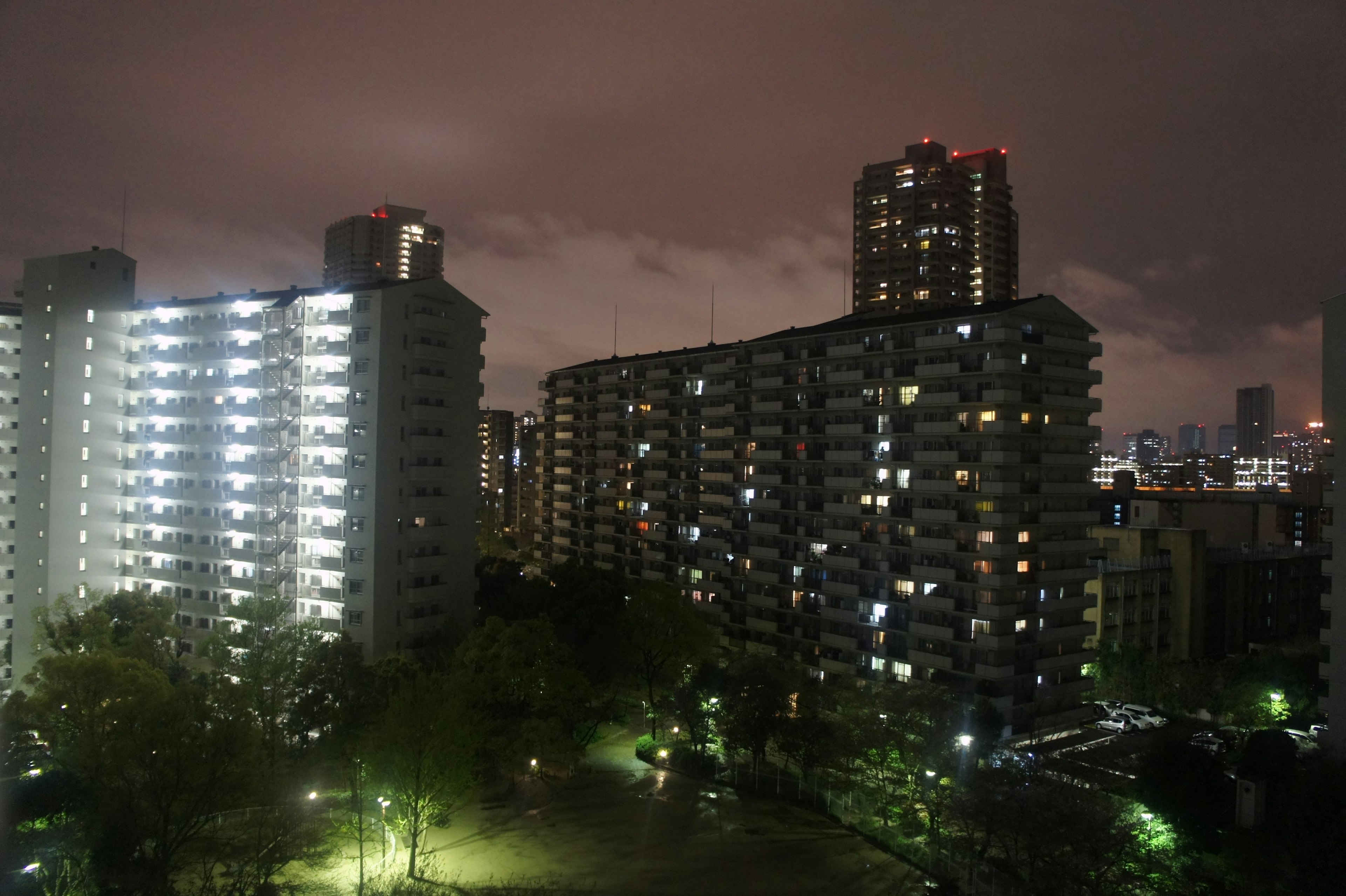 Pemandangan malam gedung apartemen dengan jendela yang menyala dan taman hijau