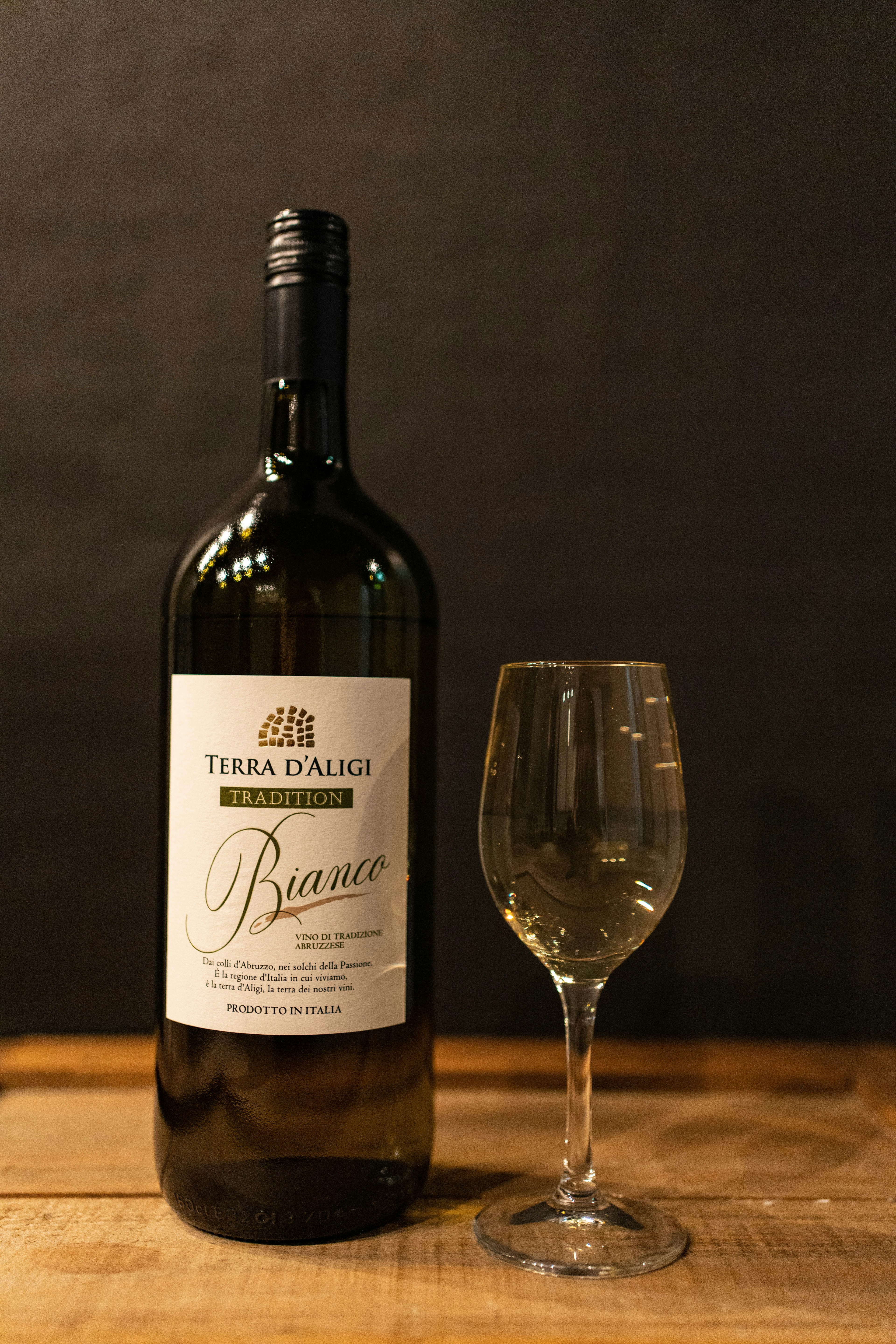 A bottle of white wine and a wine glass placed on a wooden table