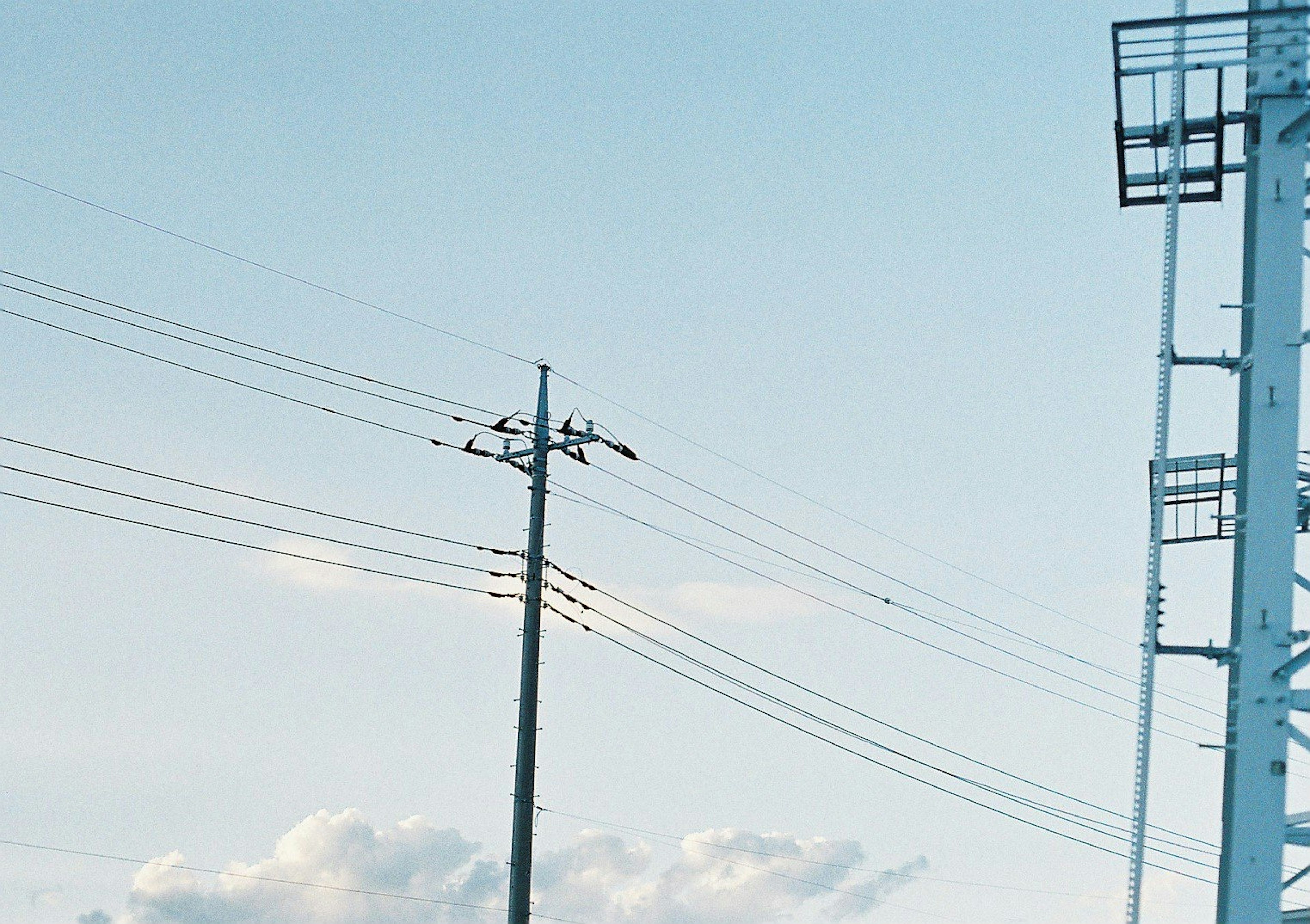 Un paysage avec un poteau électrique et des lignes à haute tension sous un ciel bleu