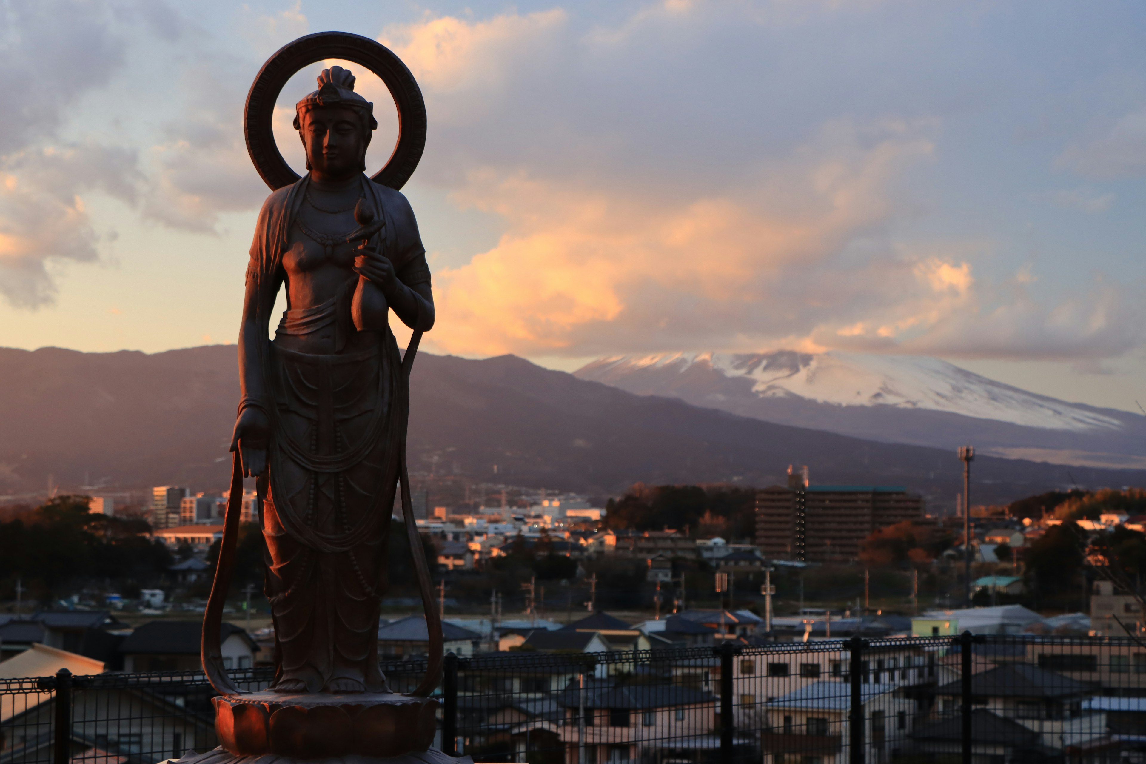 Kannon statue standing against a sunset with a snow-capped mountain in the background