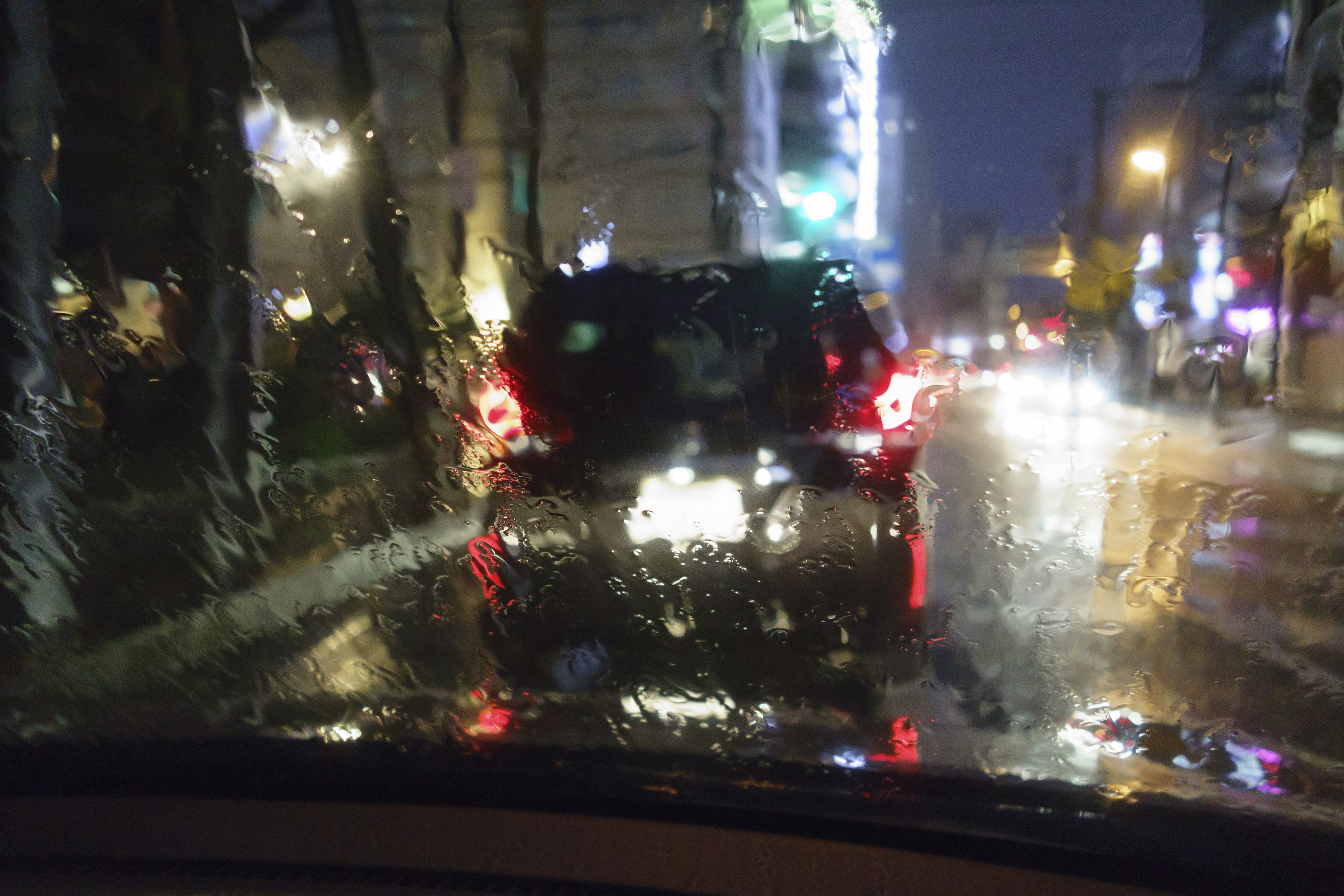 Scène nocturne de la ville sous la pluie vue à travers un pare-brise de voiture avec des gouttes d'eau