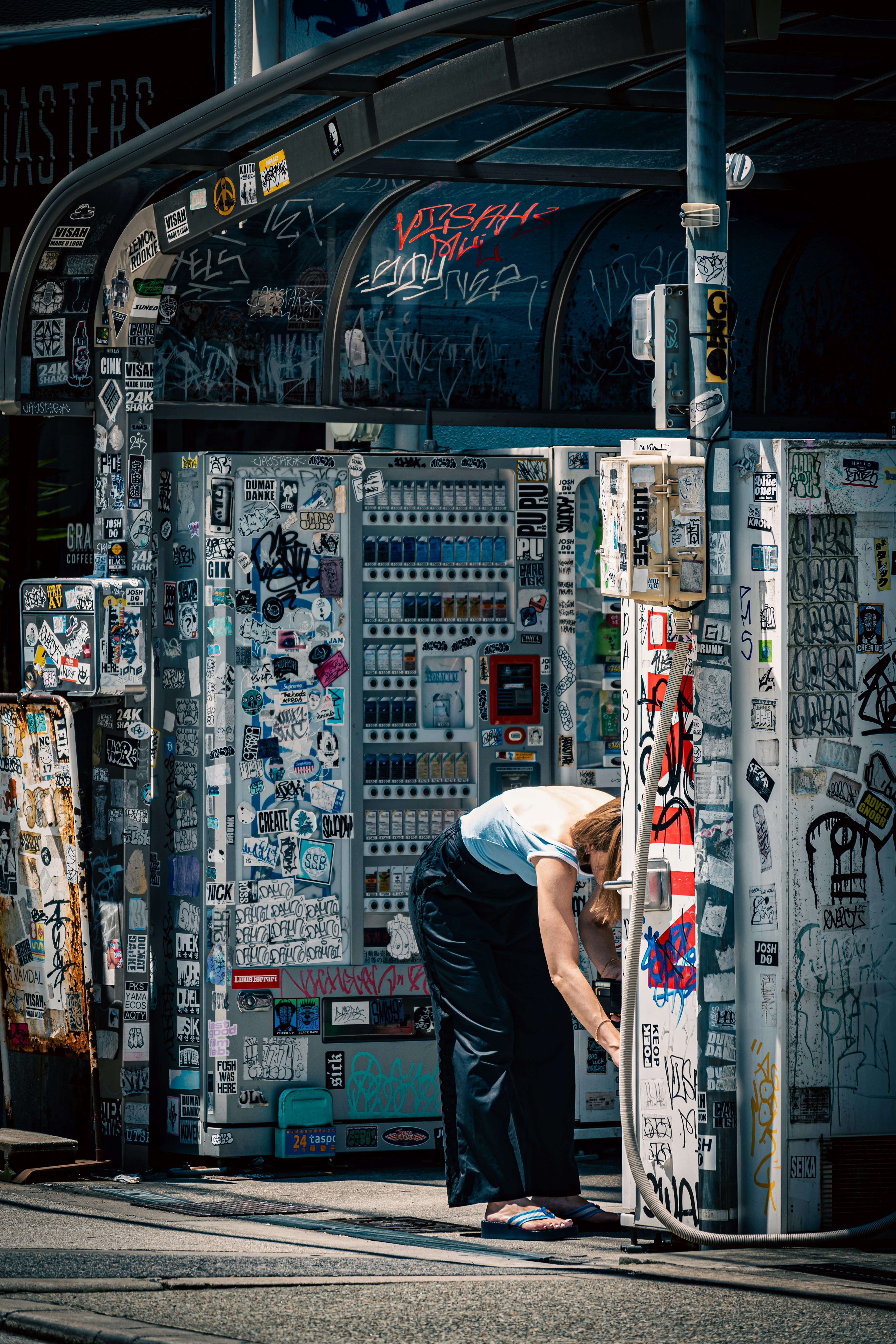 Mujer trabajando frente a una cabina telefónica cubierta de arte callejero