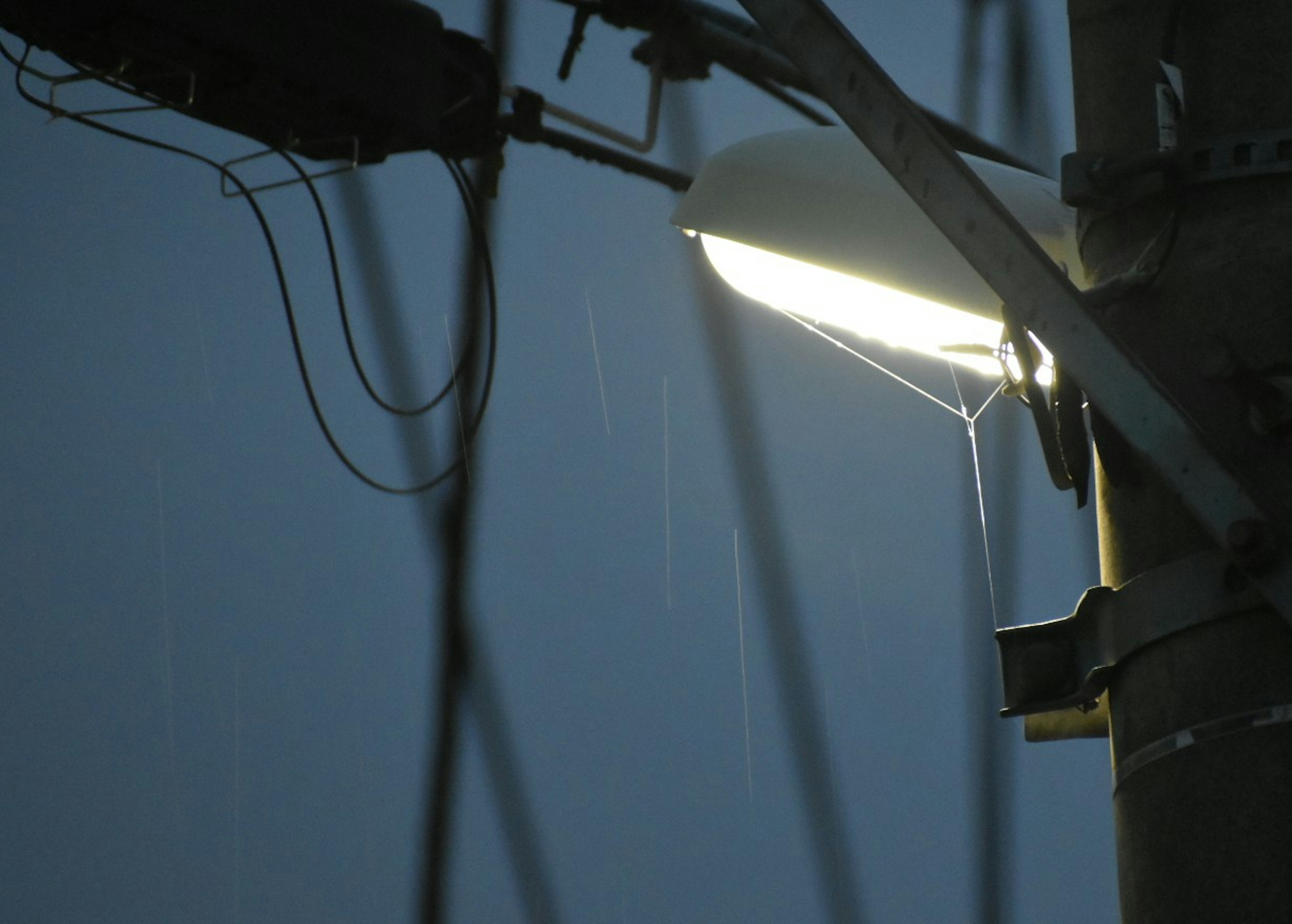 Gros plan d'un lampadaire brillant sous la pluie avec des fils électriques