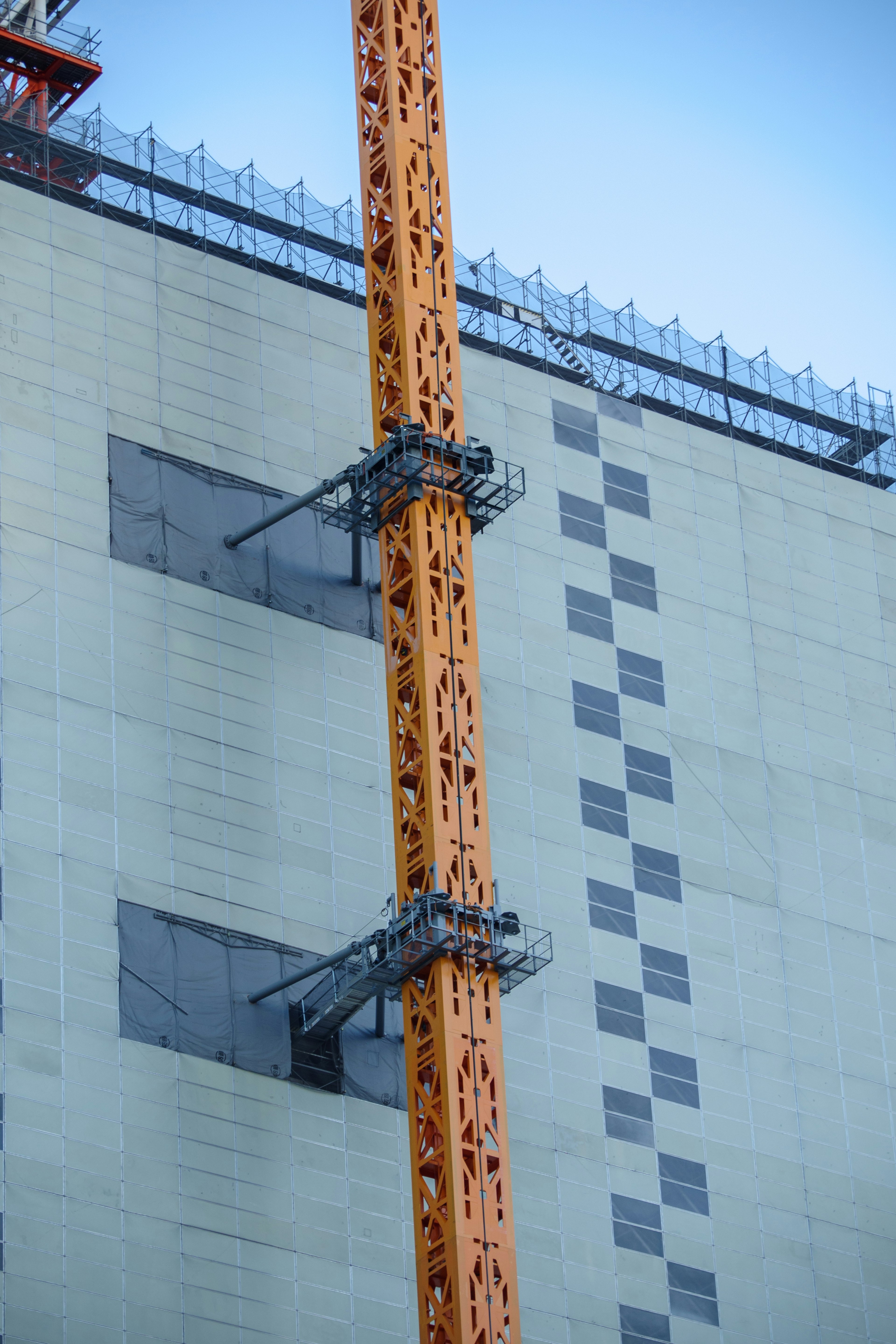 Orange construction crane attached to the exterior of a building under construction