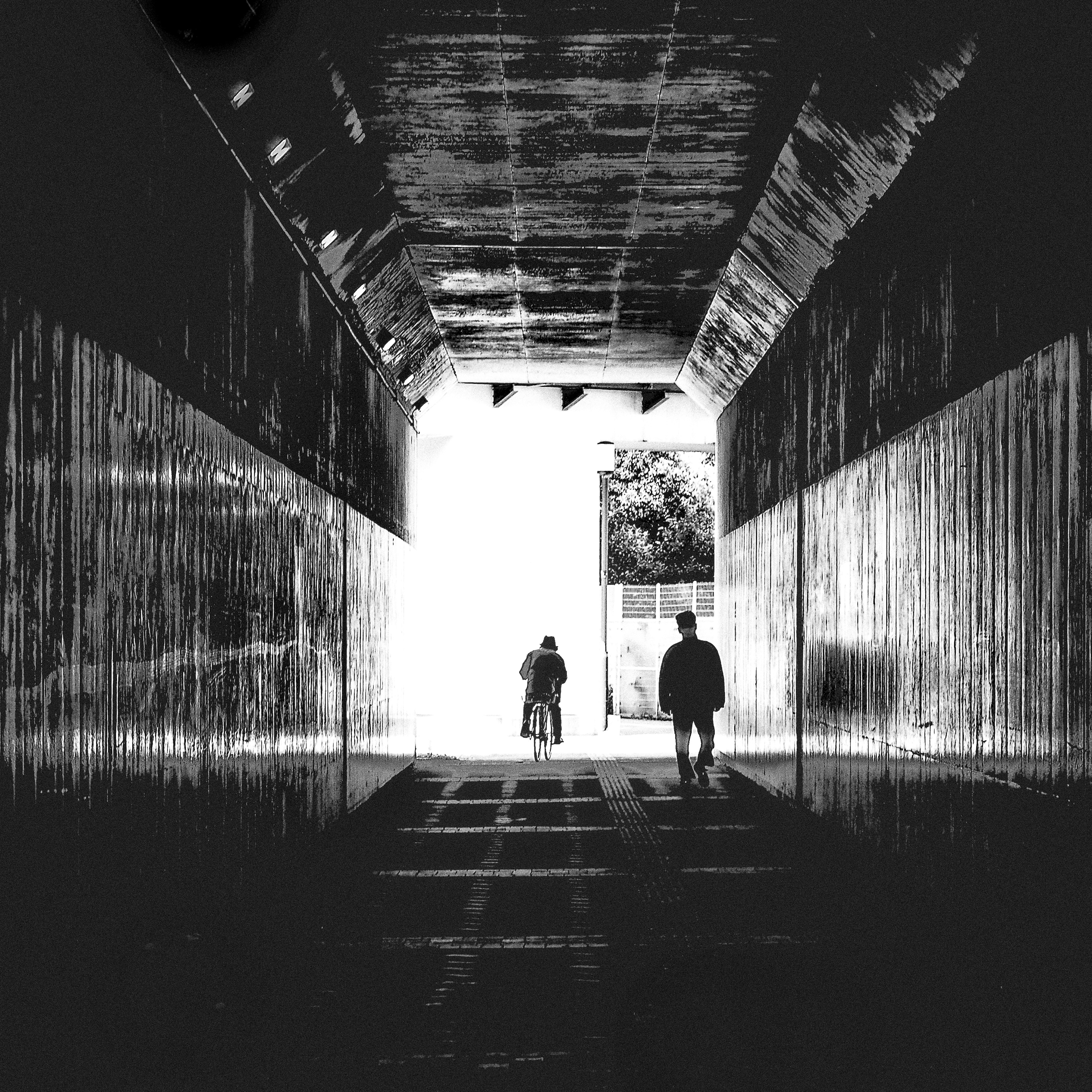 Deux silhouettes marchant dans un tunnel sombre avec une sortie lumineuse visible