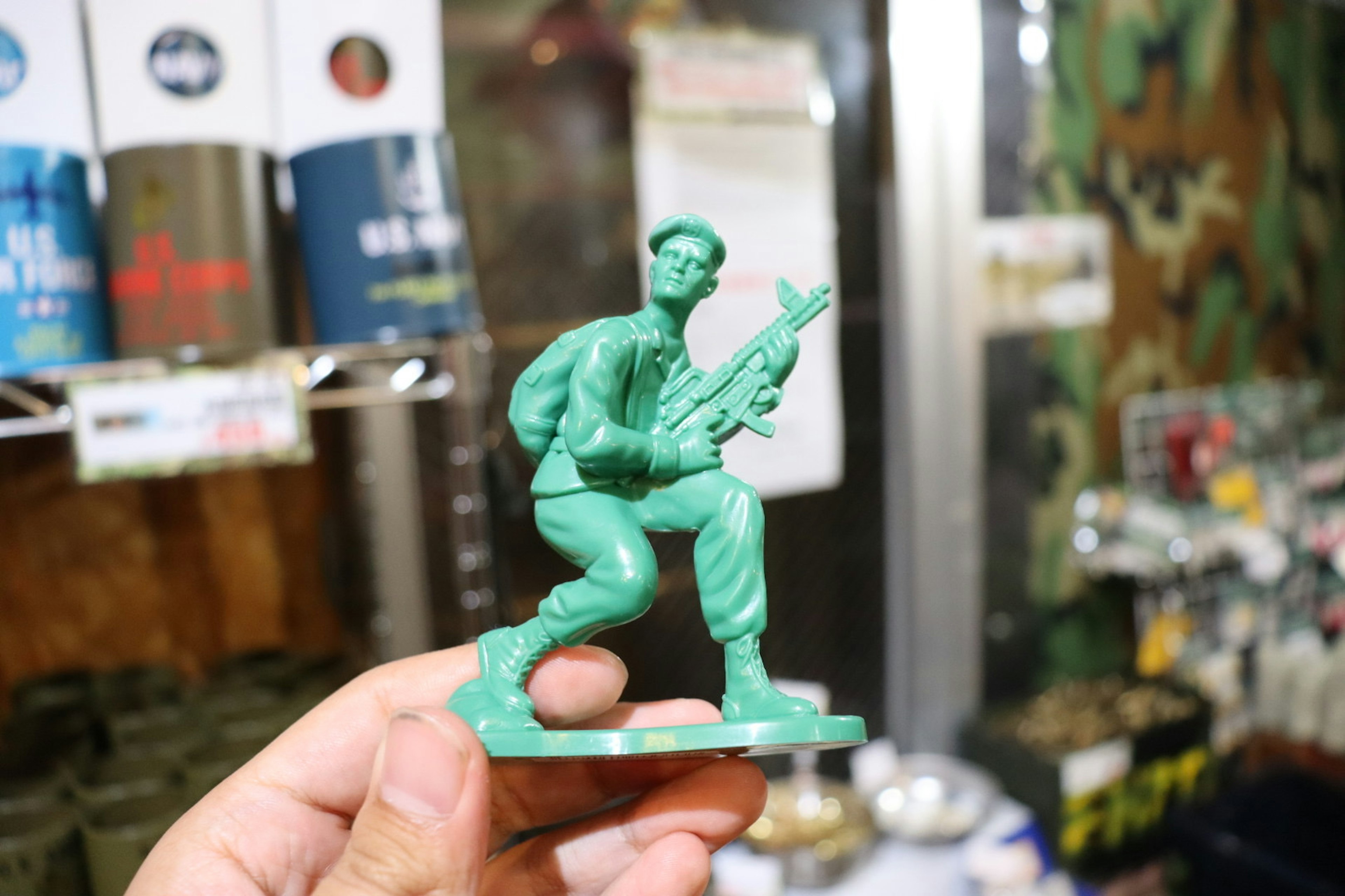 Main tenant une figurine de soldat verte avec un fond camouflage et des articles militaires