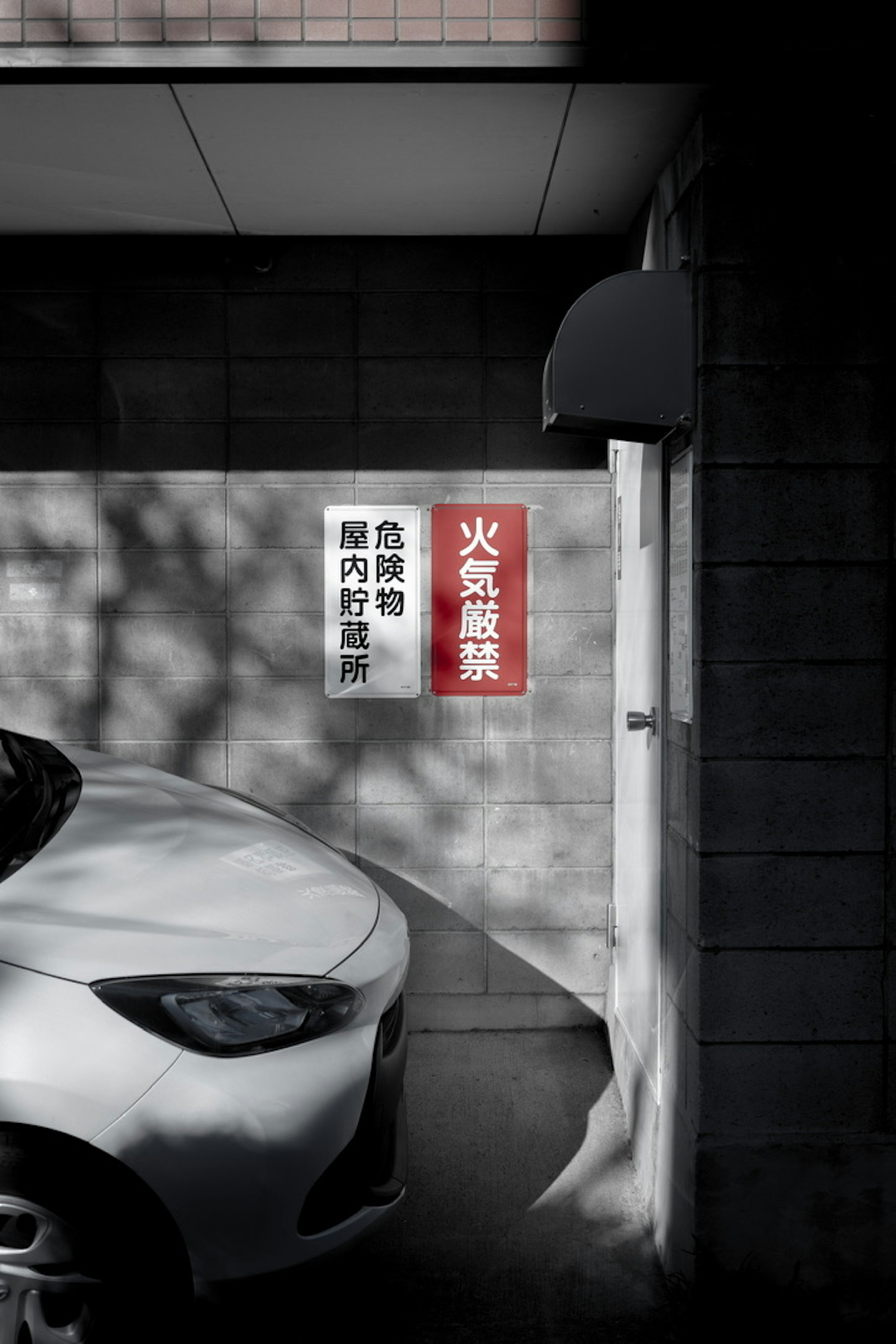 A corner of a parking area featuring a white car and a red sign on the wall