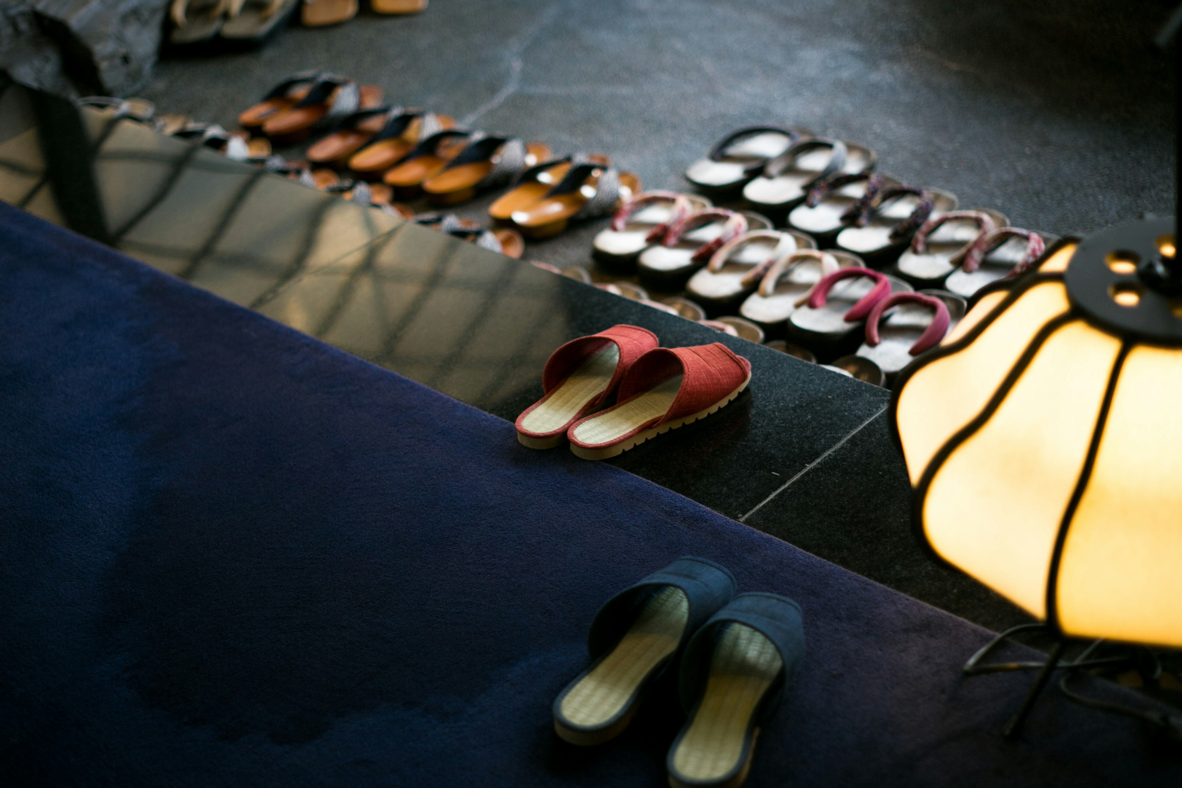 Red and blue slippers in the foreground with a line of sandals in the background in a well-lit room