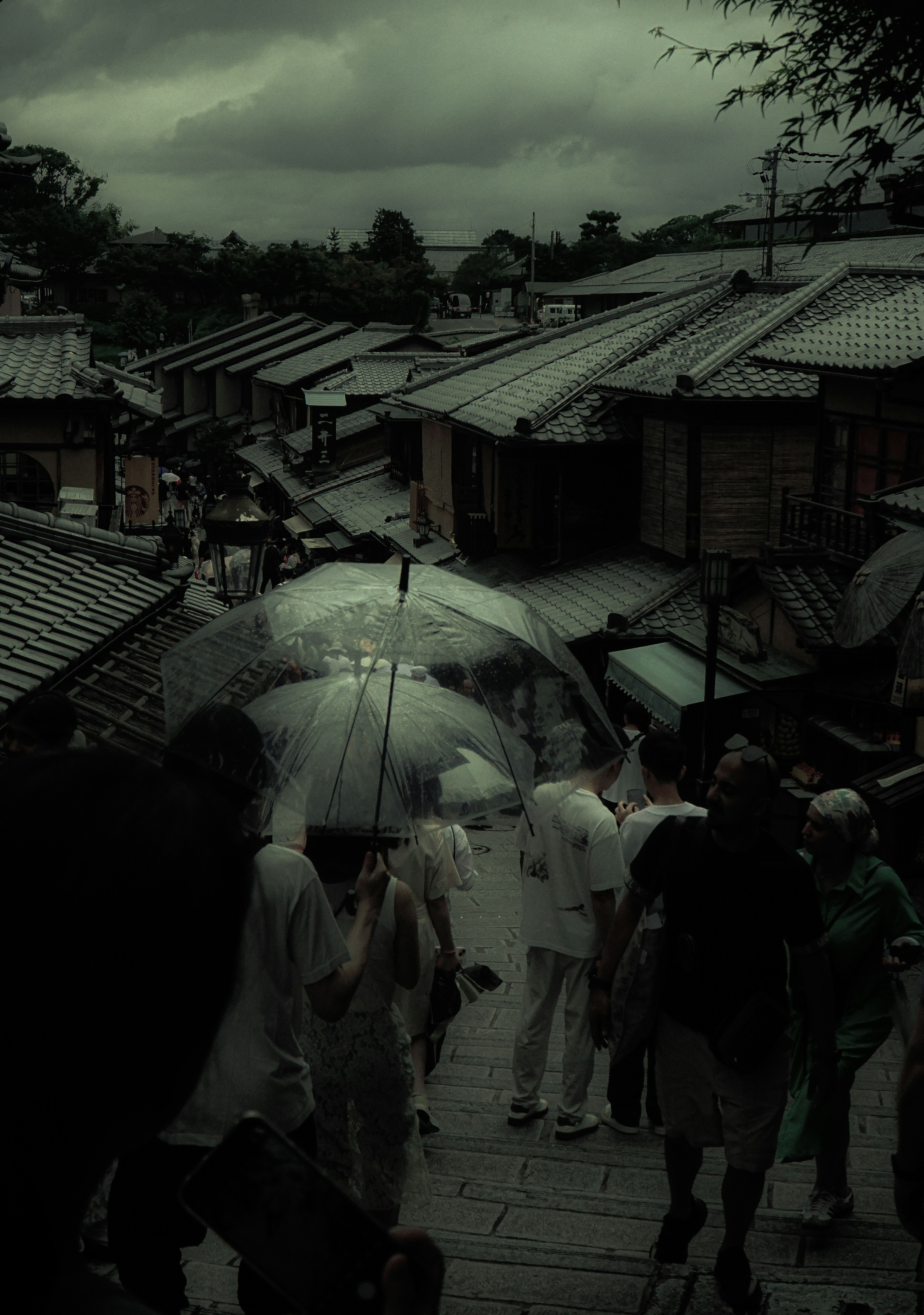 People walking with umbrellas in an old street under a cloudy sky