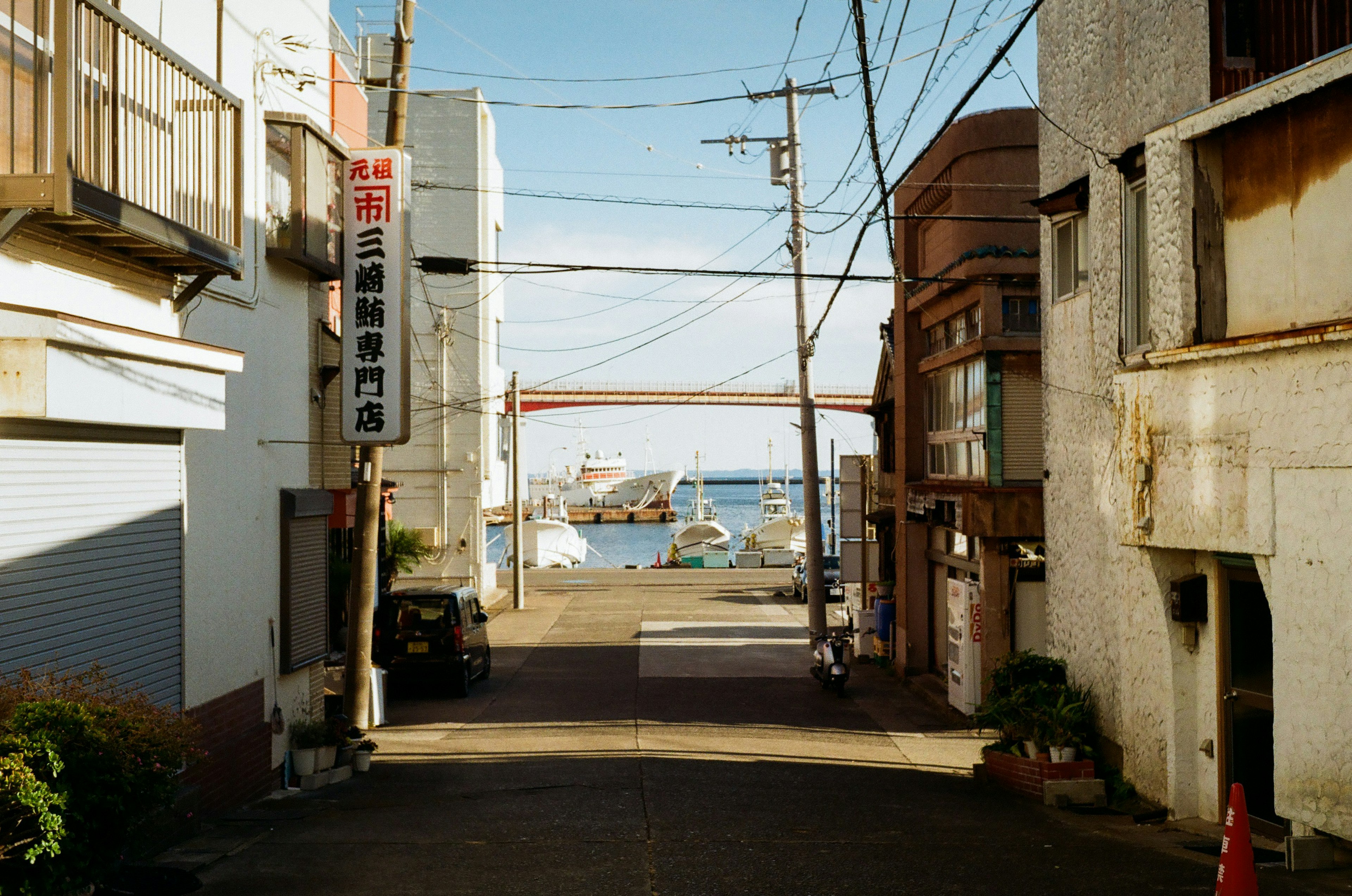 A narrow street leading to a harbor with old buildings and power lines