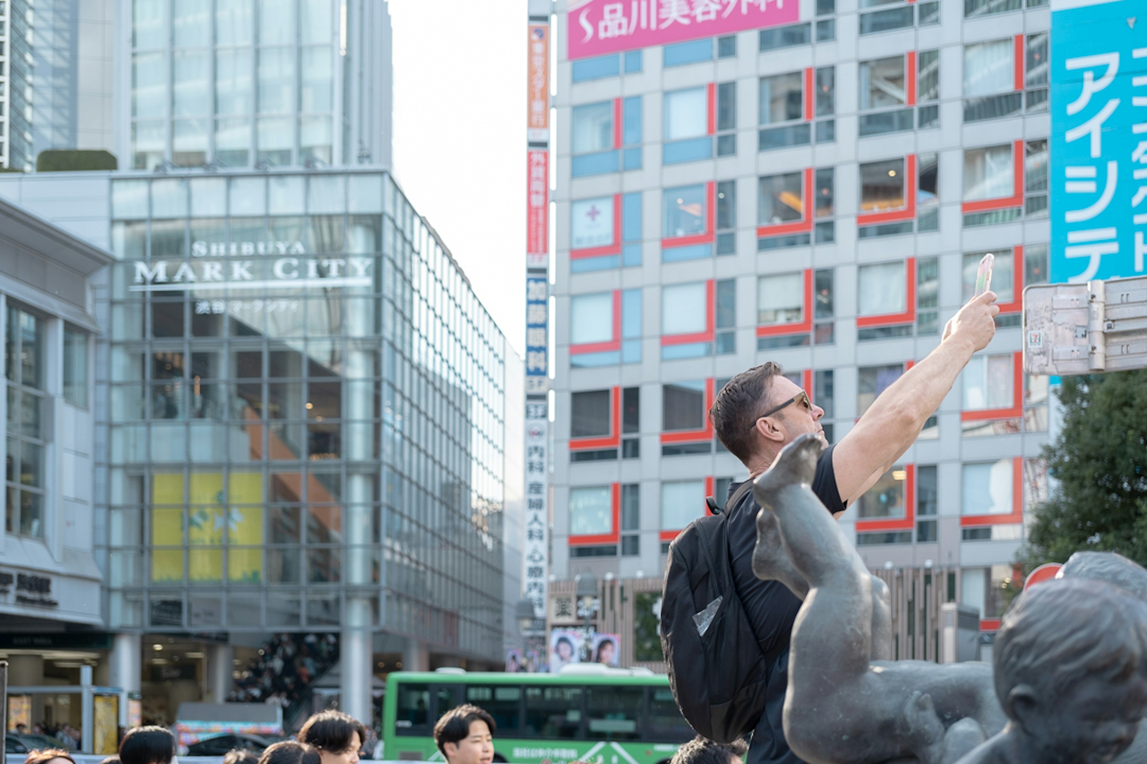 Seorang pria berpose untuk kamera di Shibuya dengan pejalan kaki dan gedung di sekitar