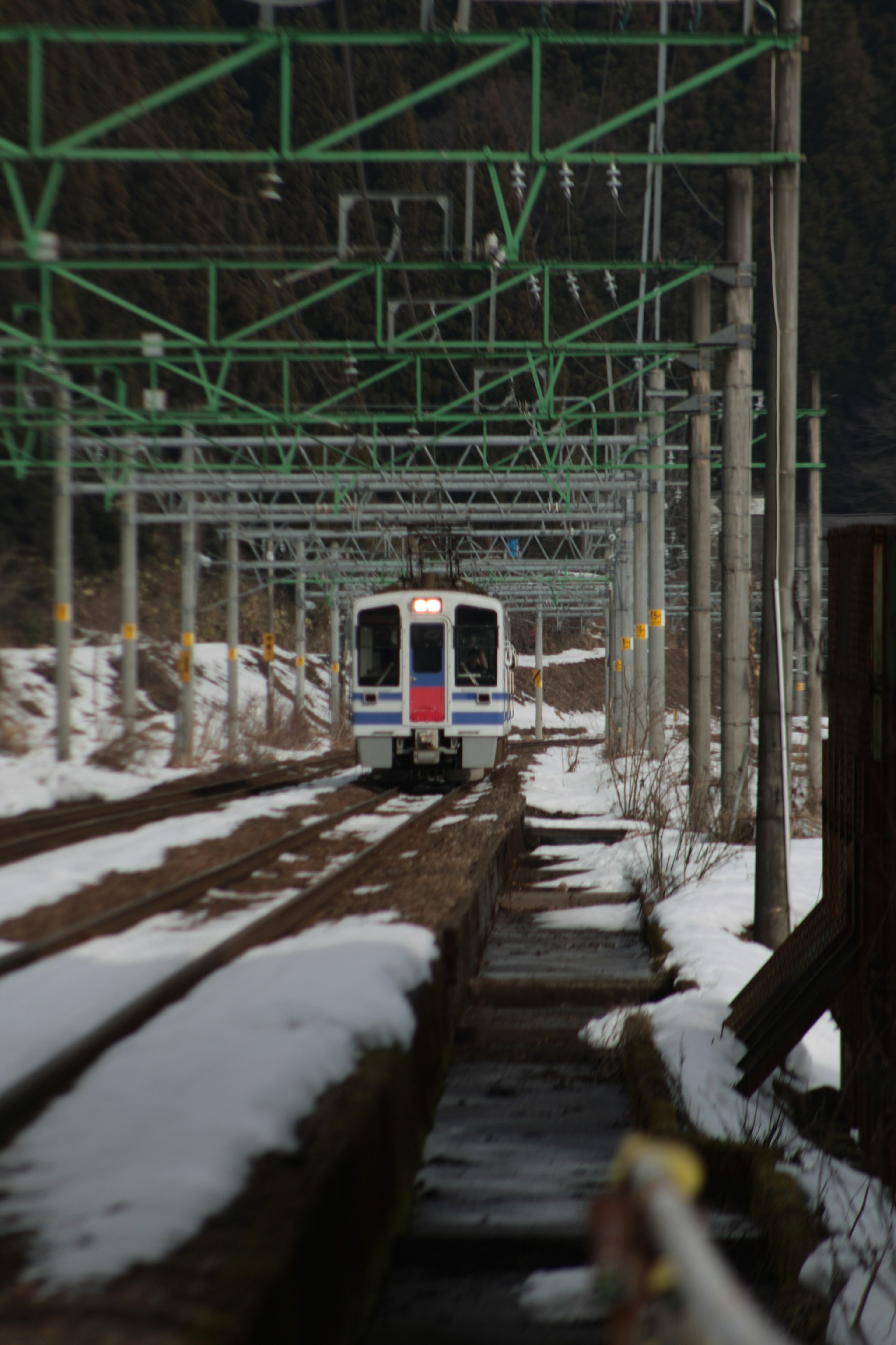 Train traveling through snow-covered tracks with green overhead lines