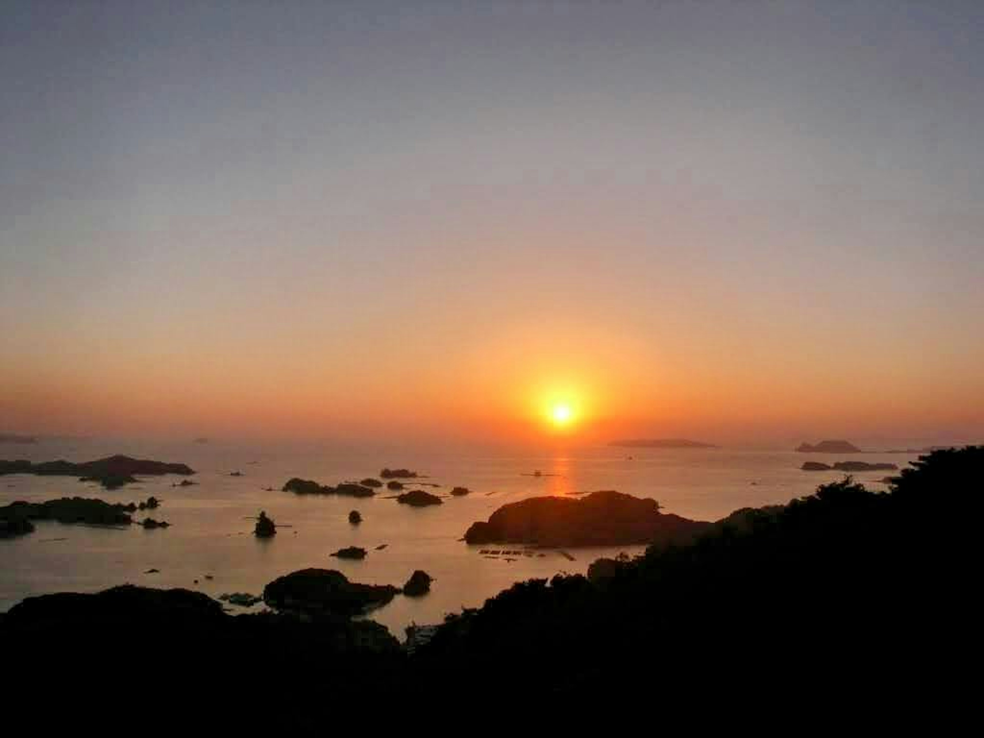 Matahari terbenam di laut dengan pulau-pulau tenang