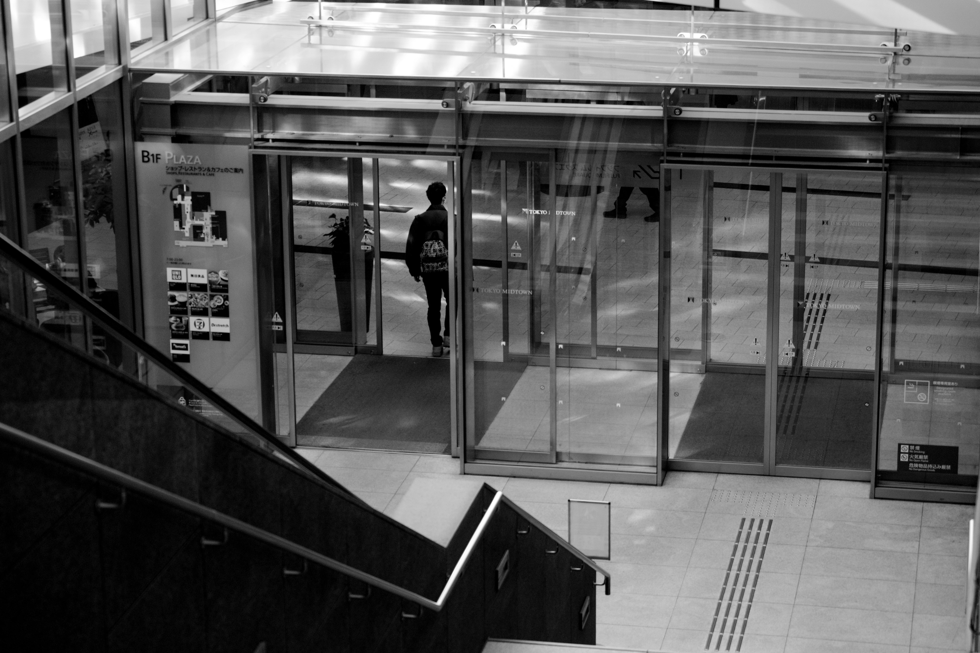 Imagen en blanco y negro de una persona caminando a través de una entrada de vidrio