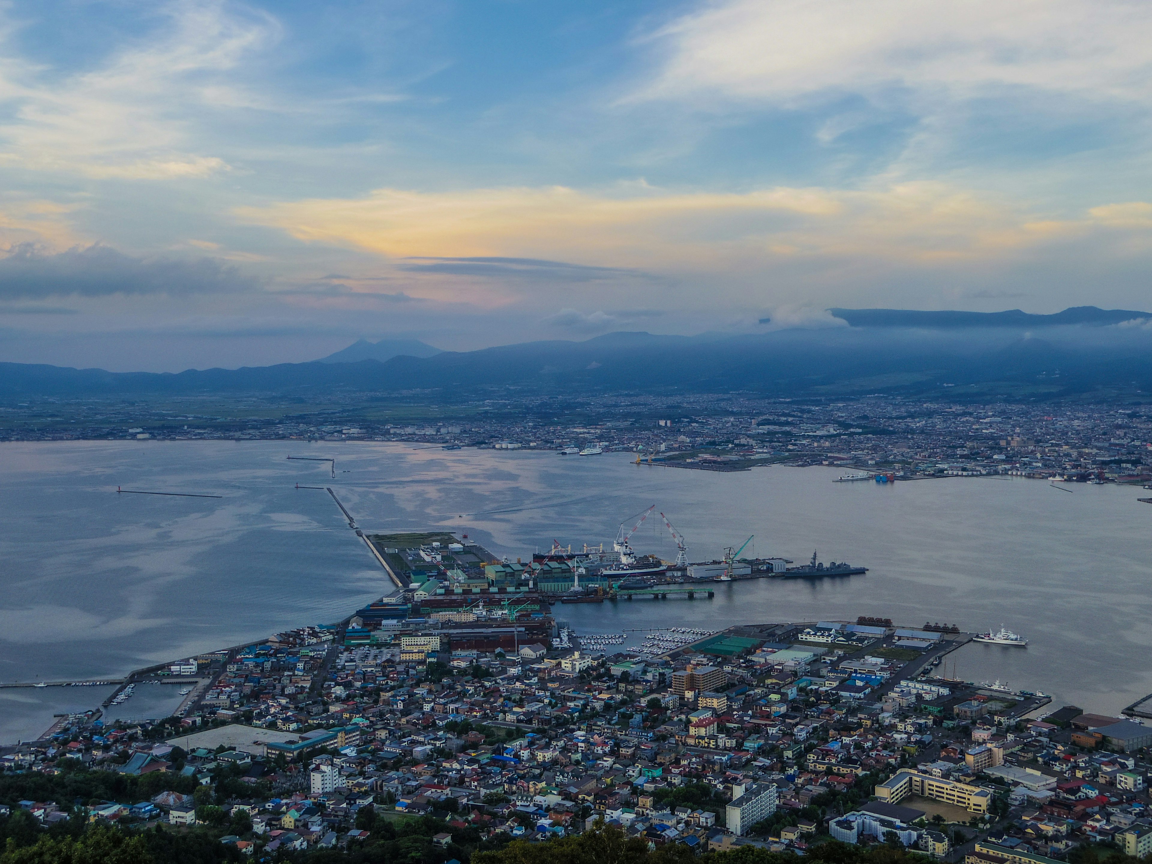 A scenic view of a coastal city at sunset with water and mountains