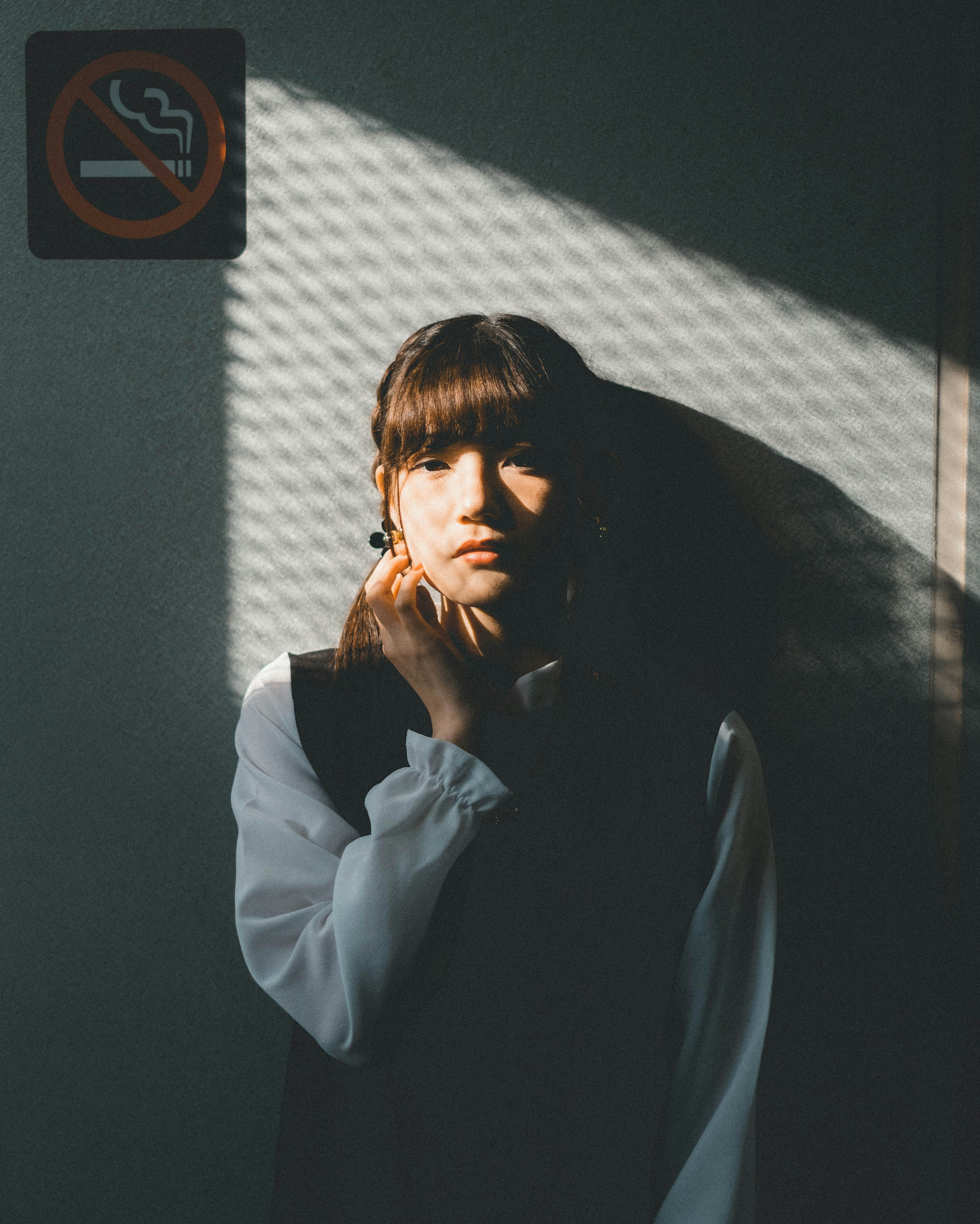 A portrait of a woman deep in thought with a no smoking sign in the background