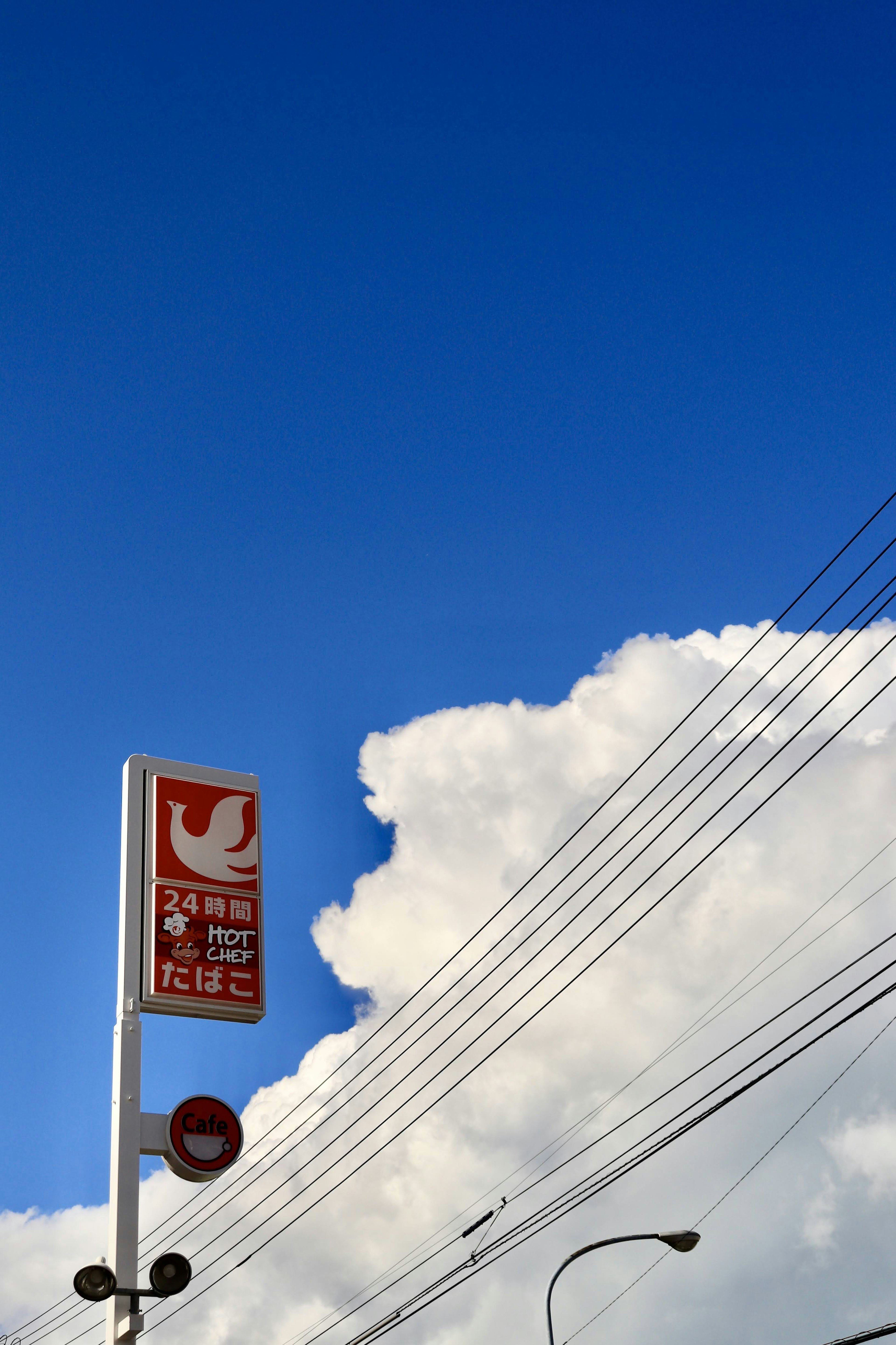 Bus stop sign against a clear blue sky with white clouds