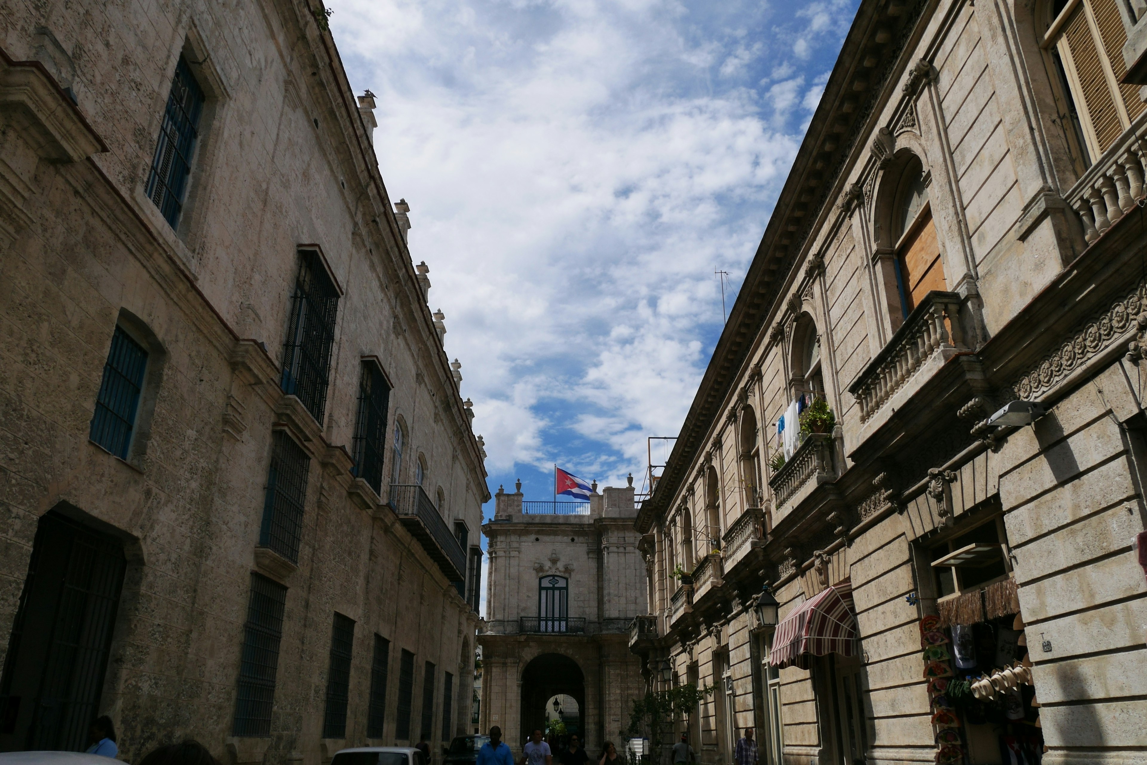 Narrow street with historical buildings and visible flag against a cloudy sky