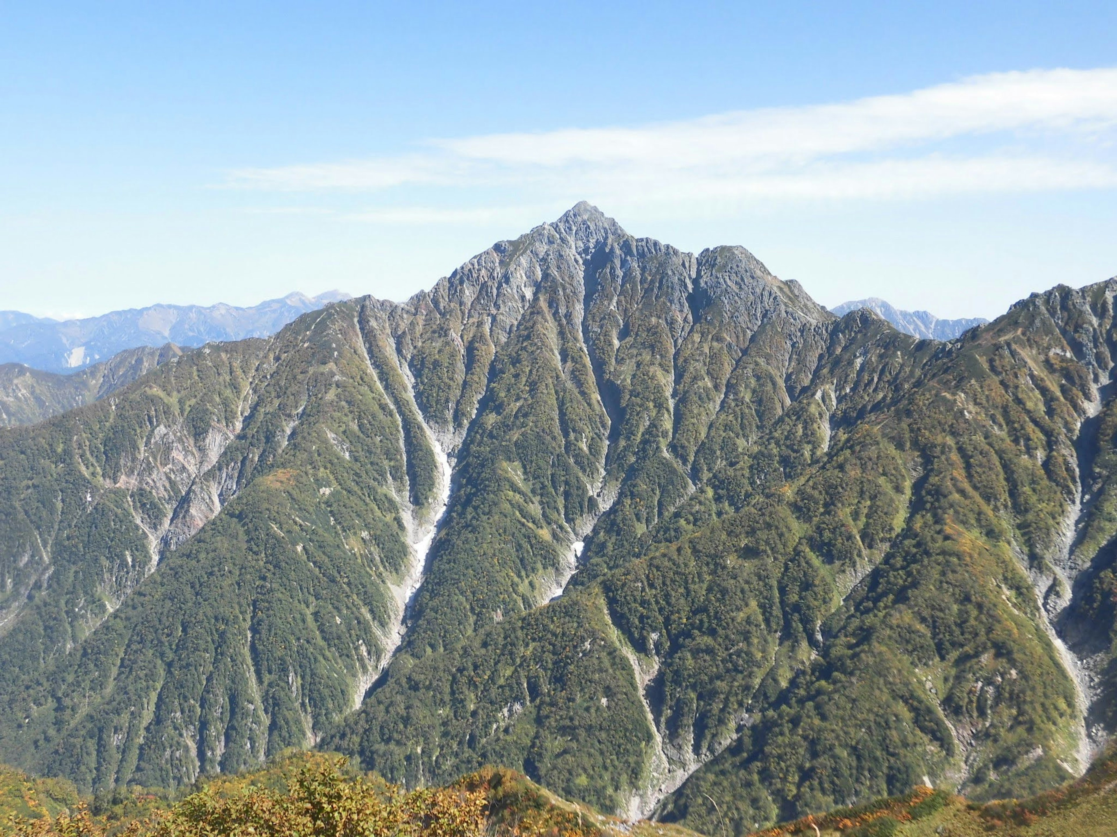 青空の下にそびえる山々の風景 緑の斜面と鋭い峰が特徴