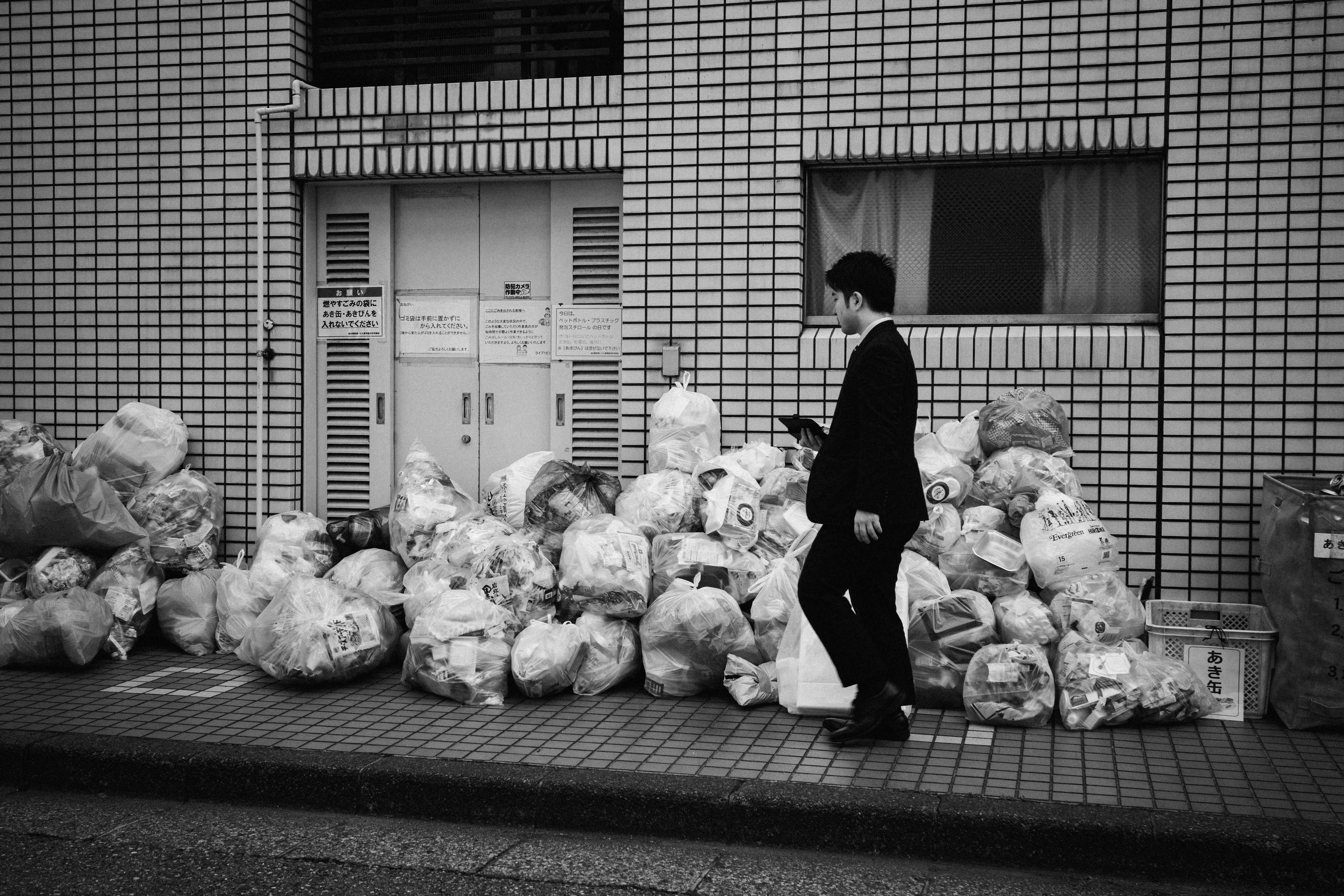 Un homme en costume marchant devant un tas de sacs poubelles contre un mur