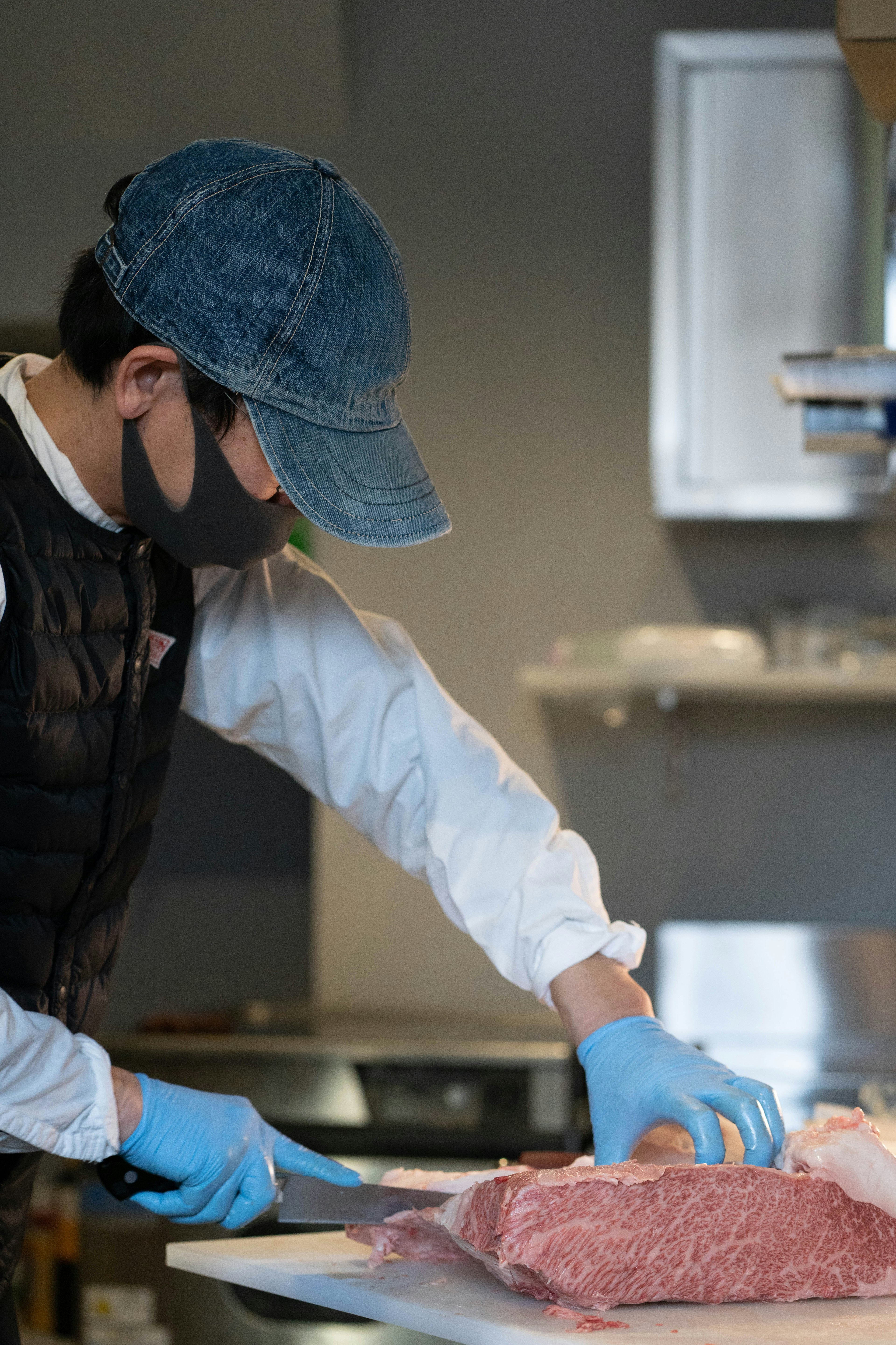 Seorang pria memotong daging mengenakan sarung tangan biru dan masker