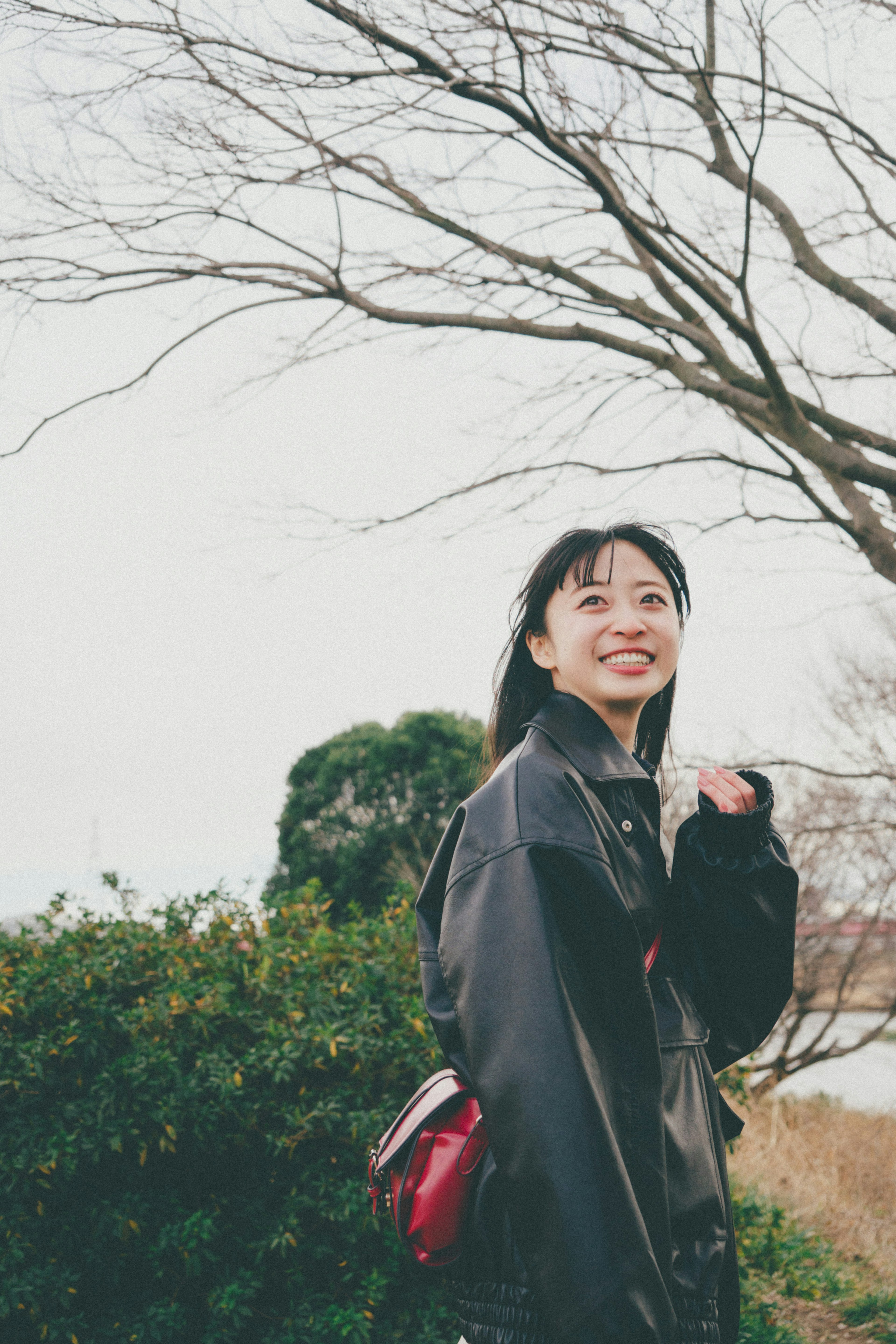 女性が笑顔で立っている風景 背景に木と緑の植物