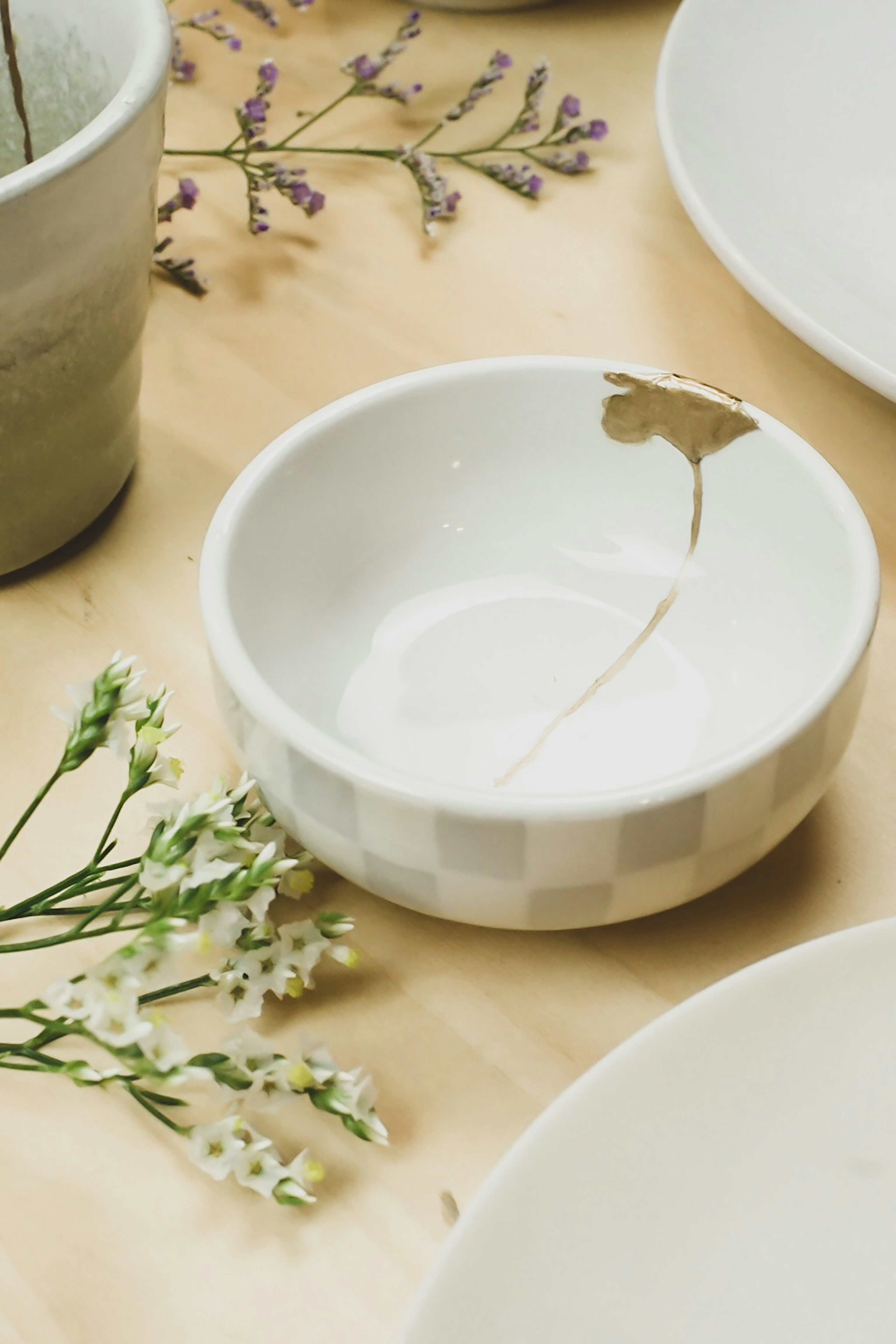 Un bol blanc avec une décoration en feuille d'or entouré de petites fleurs