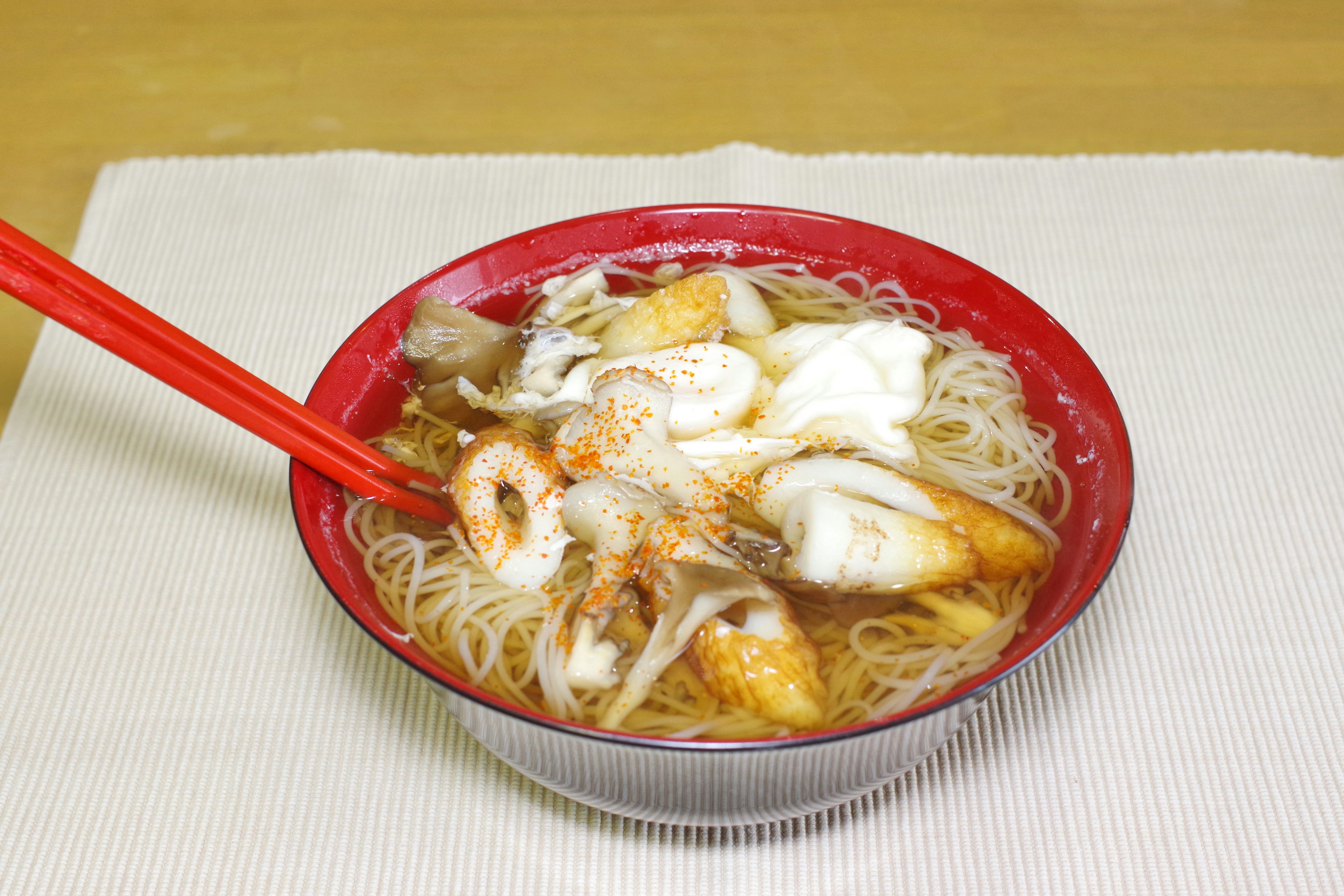 Seafood noodle soup in a red bowl with chopsticks