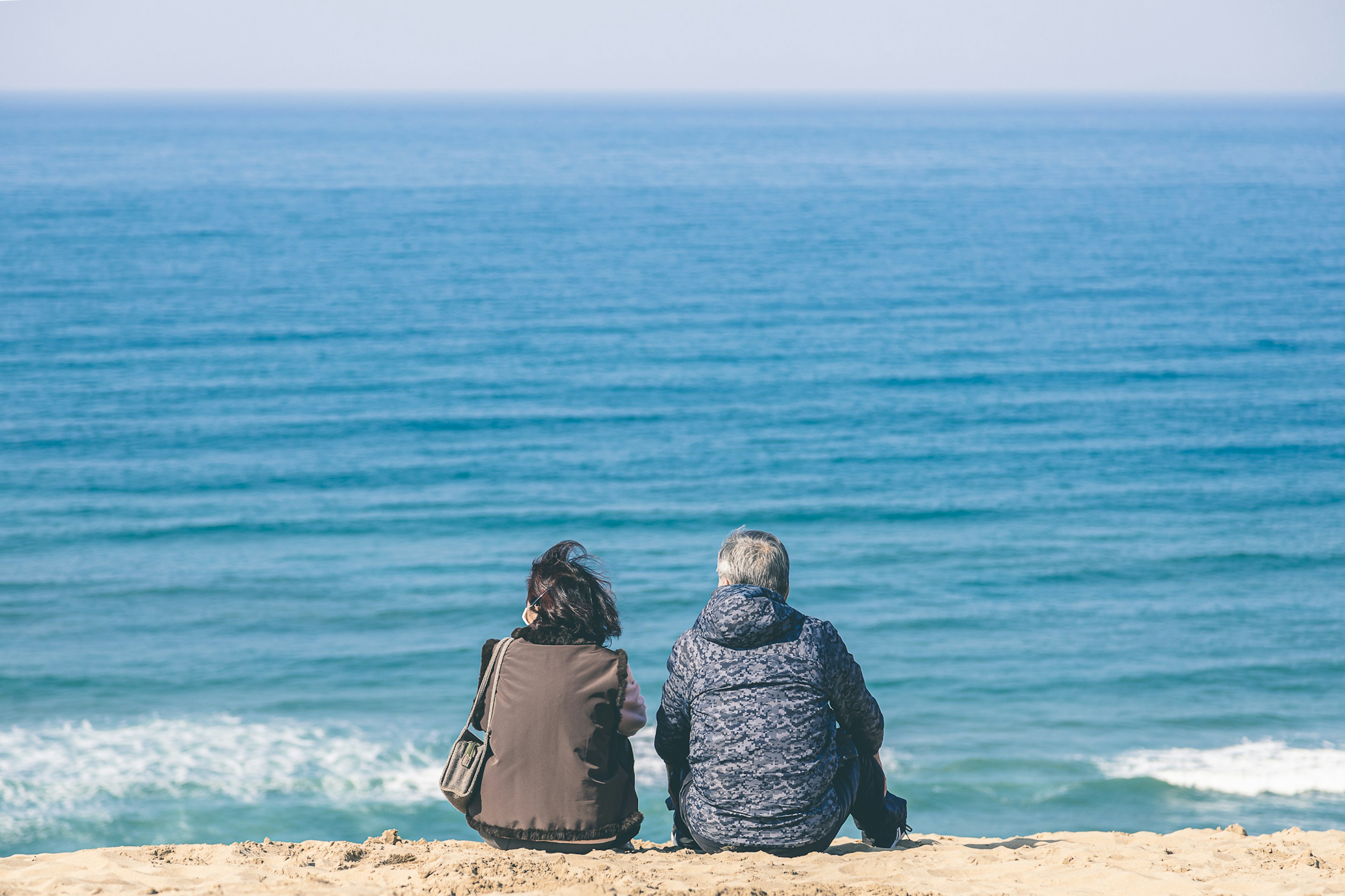 Zwei Personen sitzen am Strand und schauen auf den Ozean