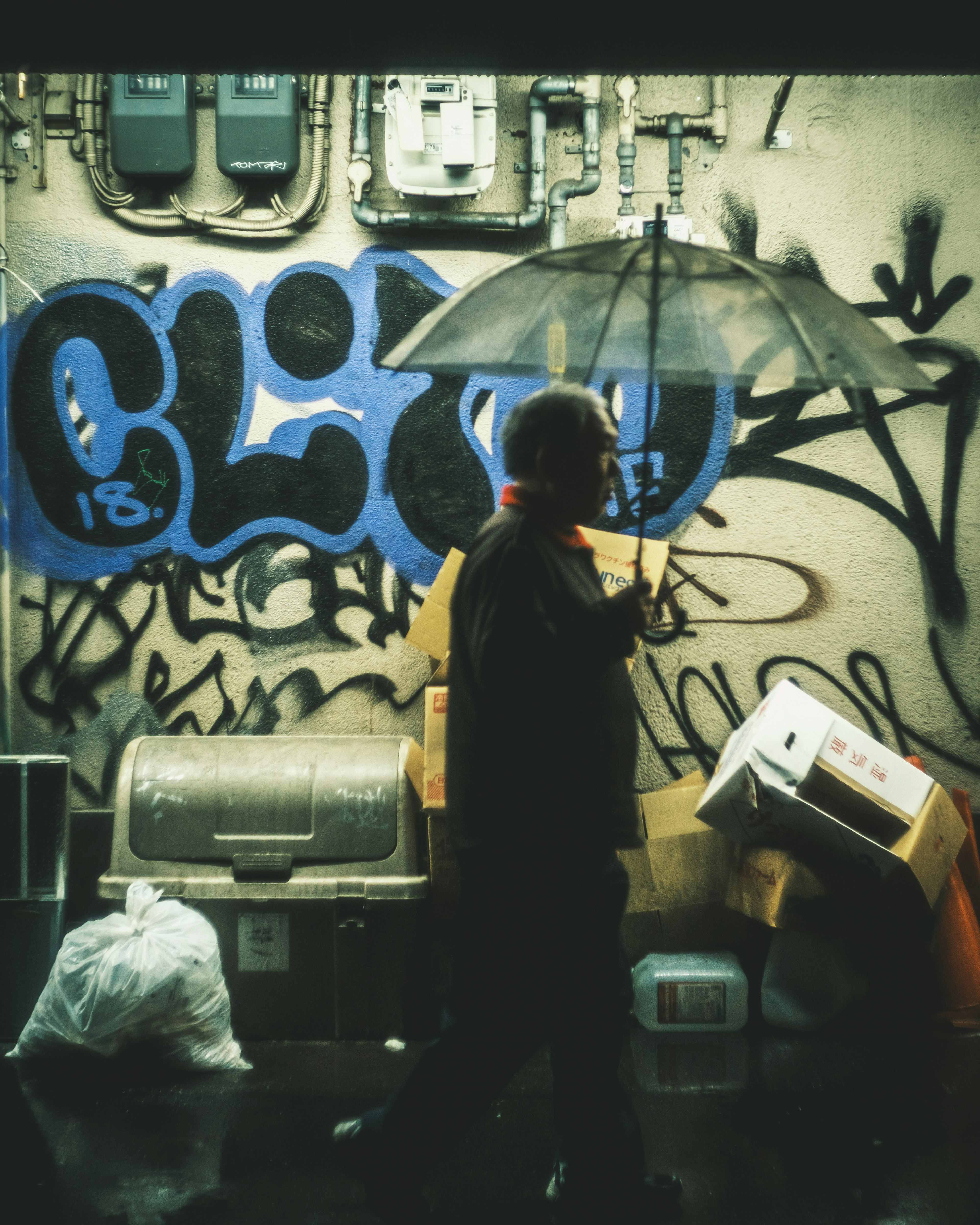 Un homme tenant un parapluie marchant devant un mur de graffiti