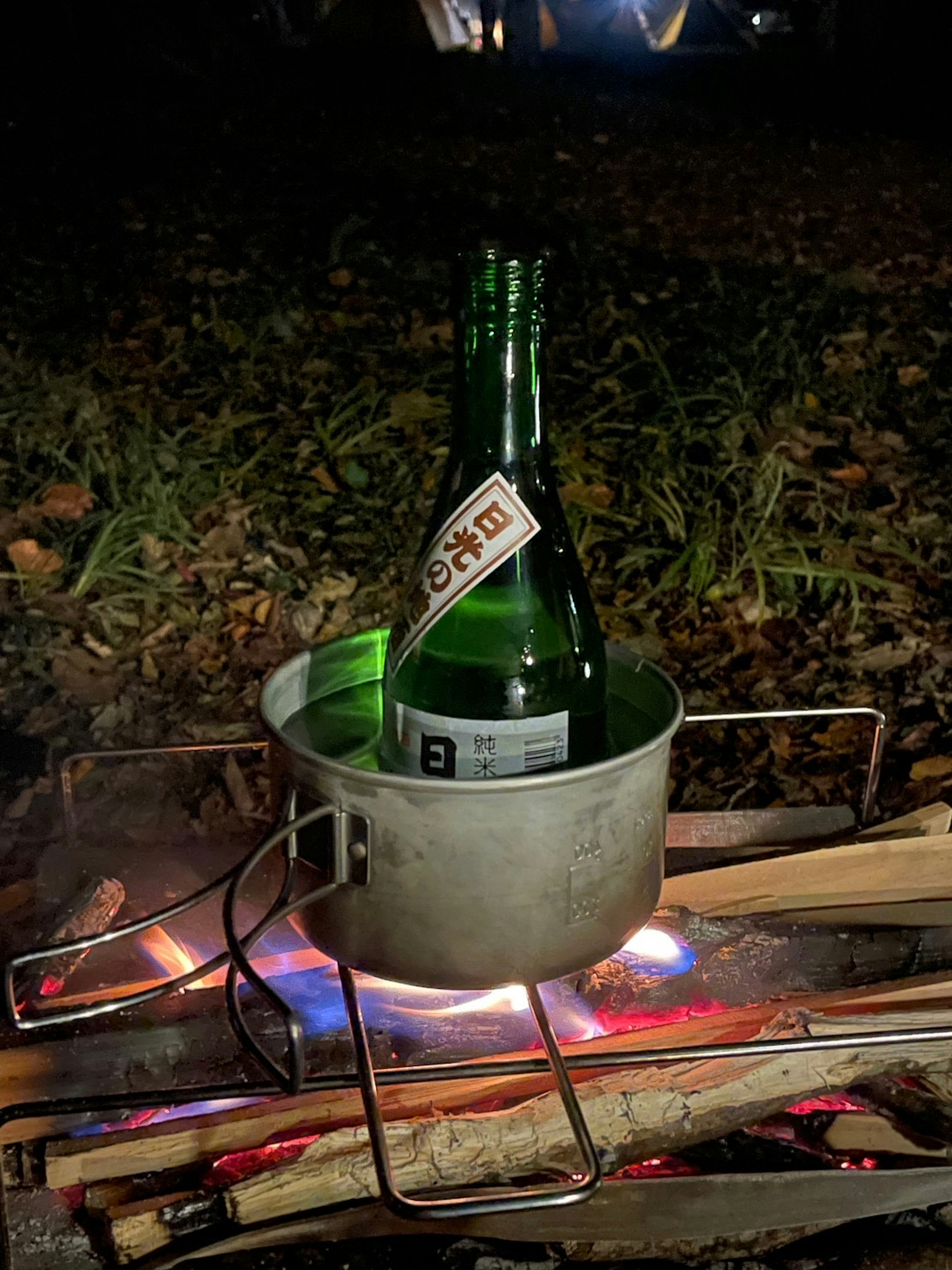 Bouteille verte placée dans une casserole au-dessus d'un feu de camp