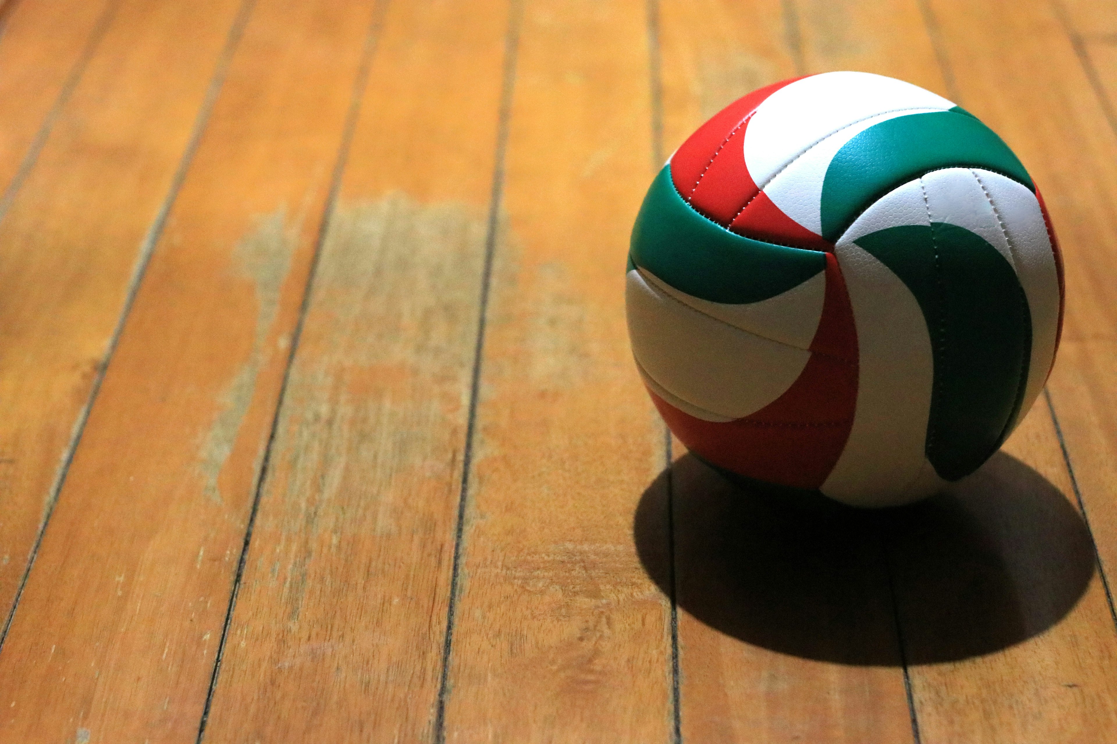 A red green and white volleyball on a wooden floor