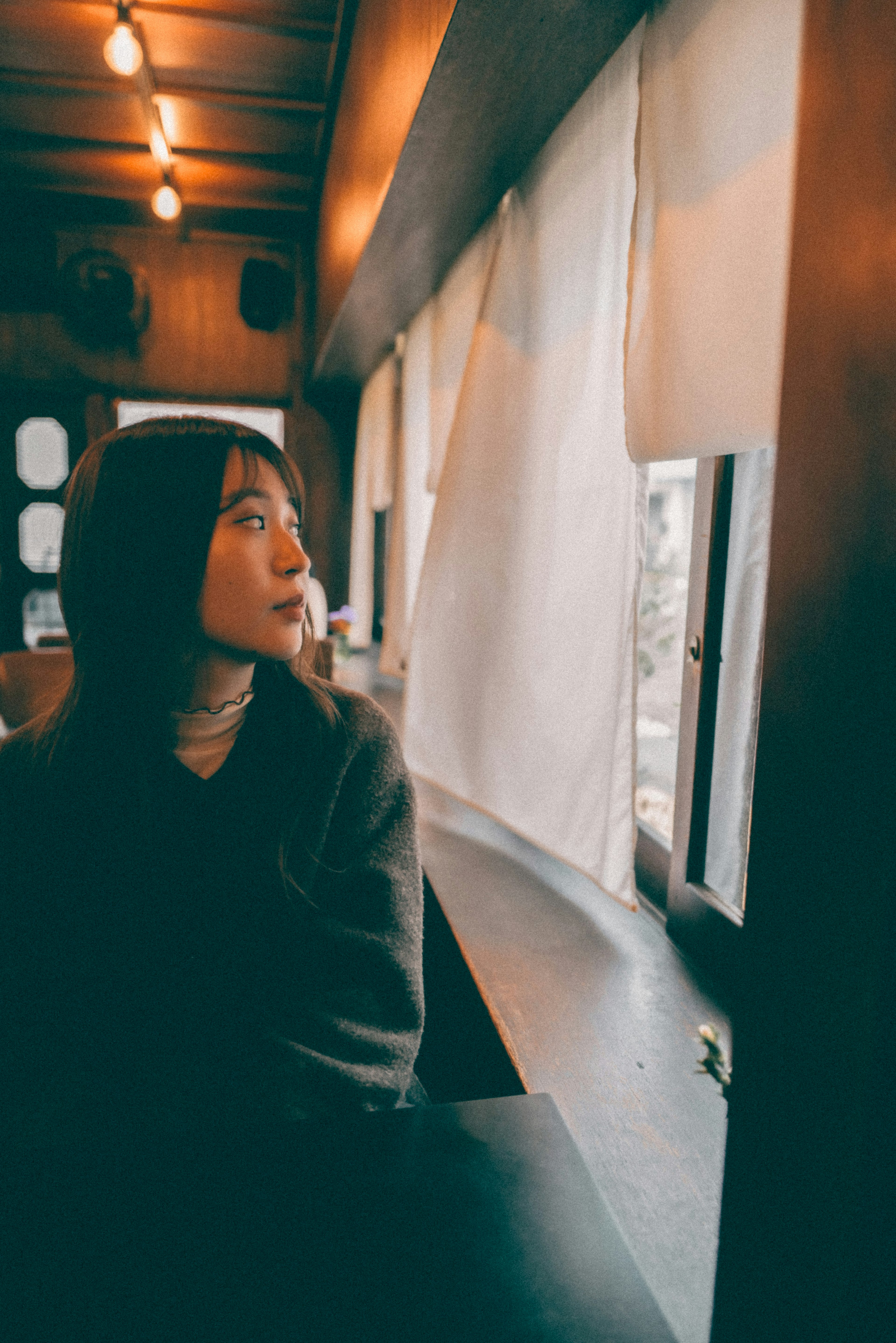 Eine Frau, die aus dem Fenster in ein gemütliches Café mit warmen Tönen schaut