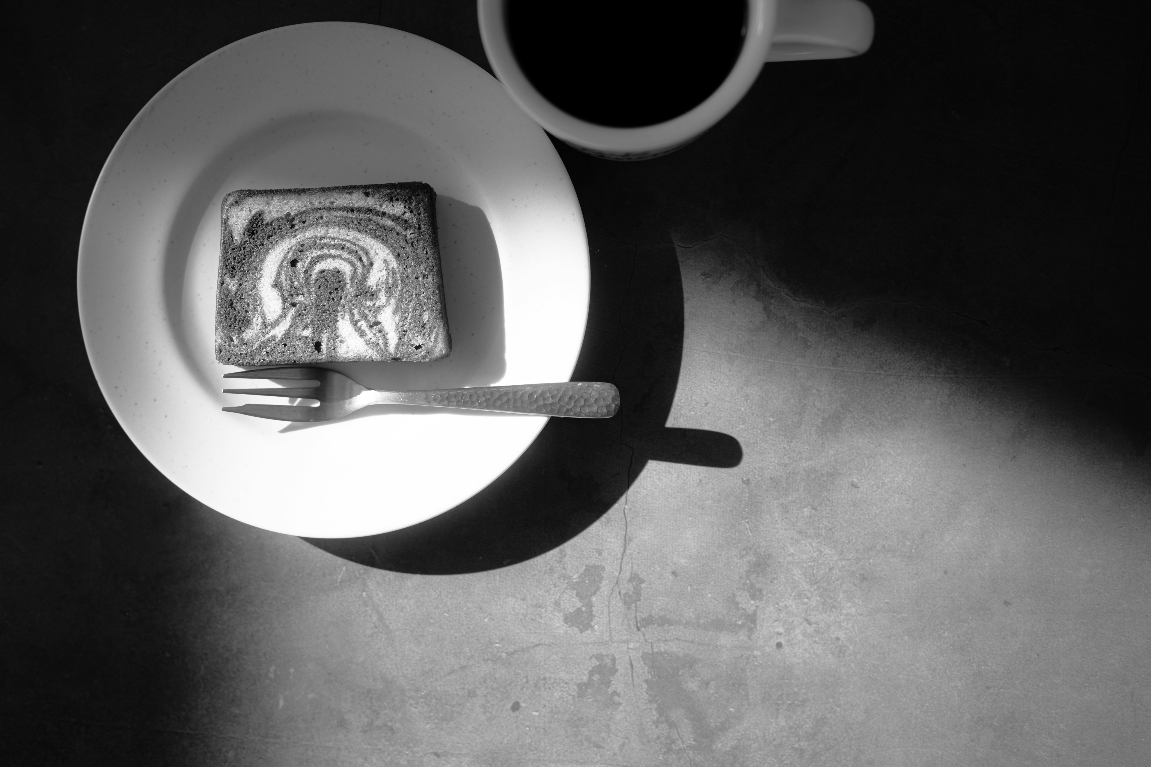 Black and white image of a coffee cup beside a dessert on a plate