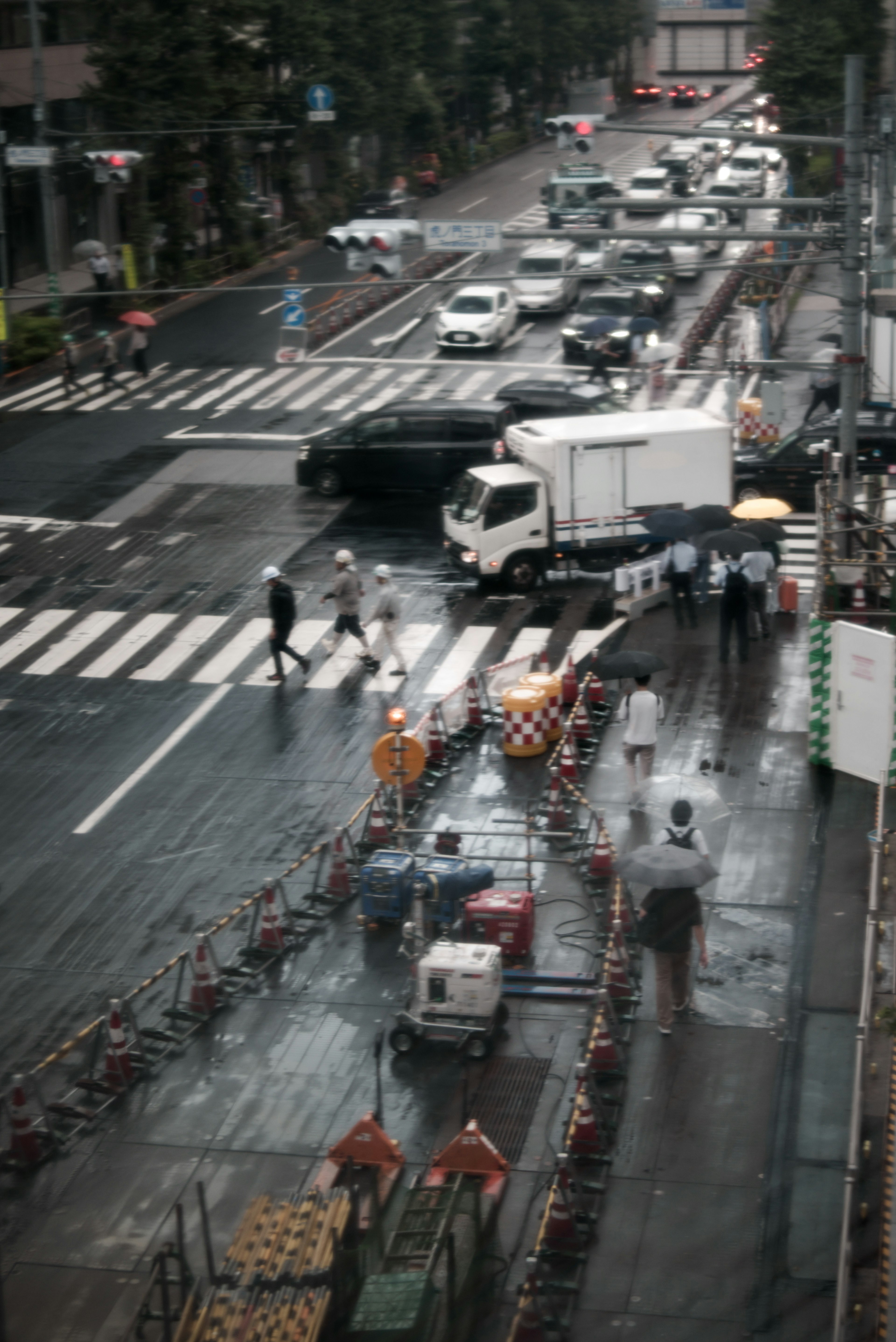 People working at a crosswalk in the rain with vehicles