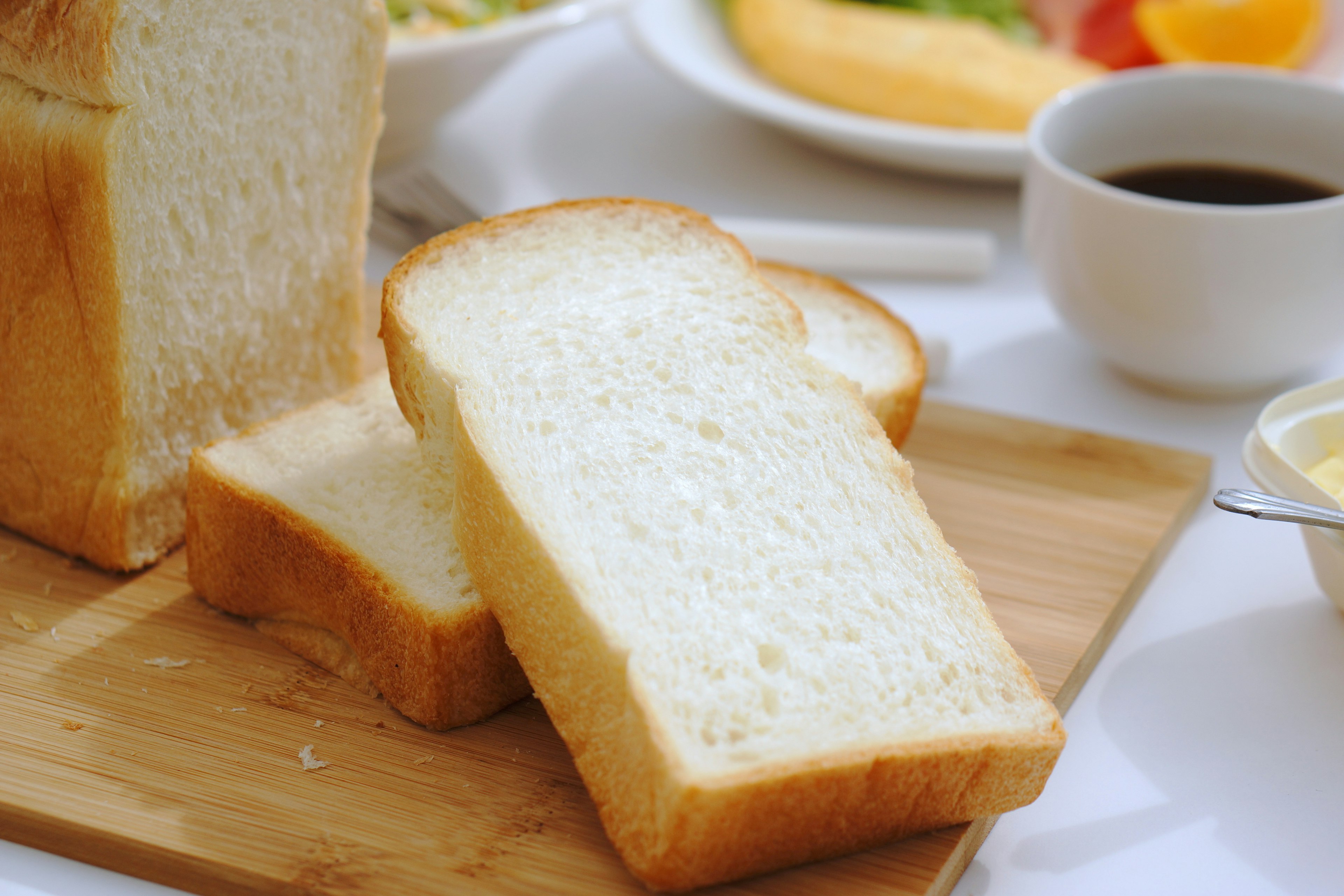 Pan en rebanadas sobre una tabla de madera con un desayuno al fondo