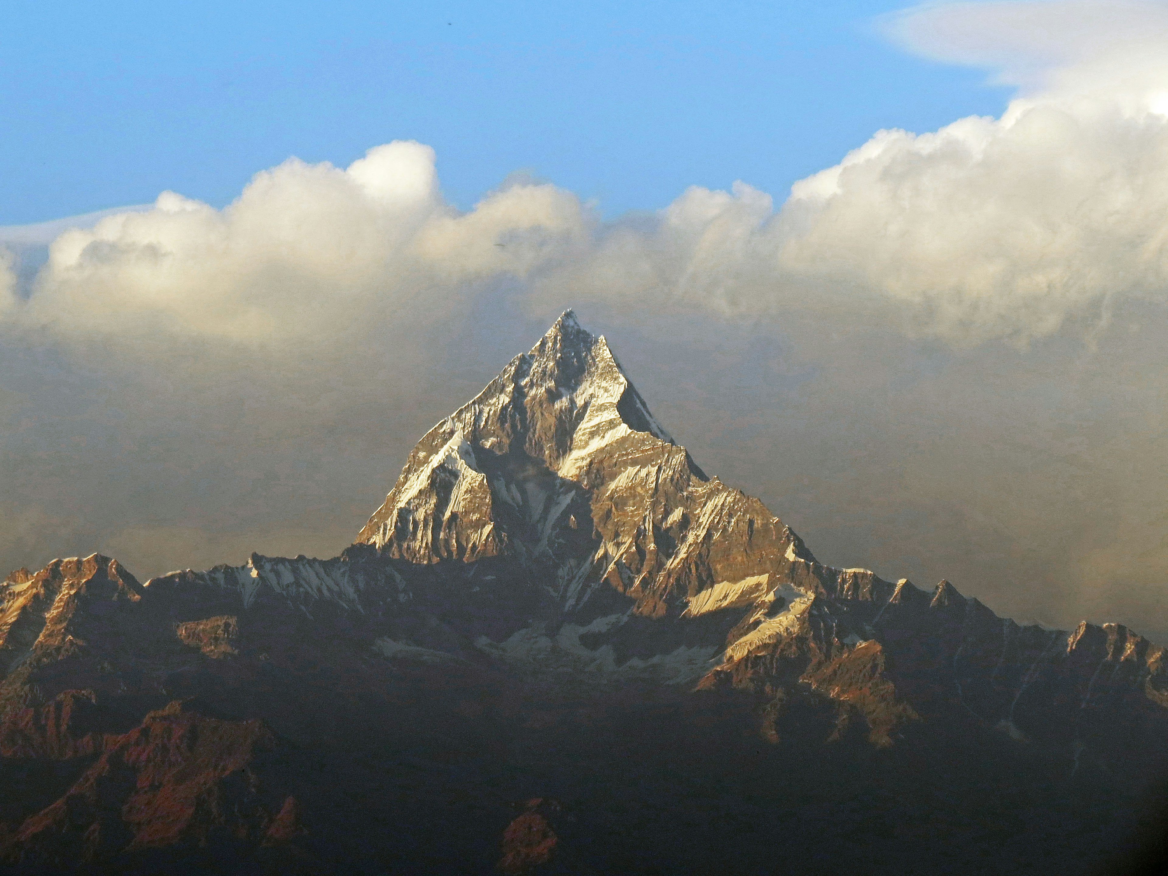 Snow-capped mountain peak surrounded by blue sky and clouds