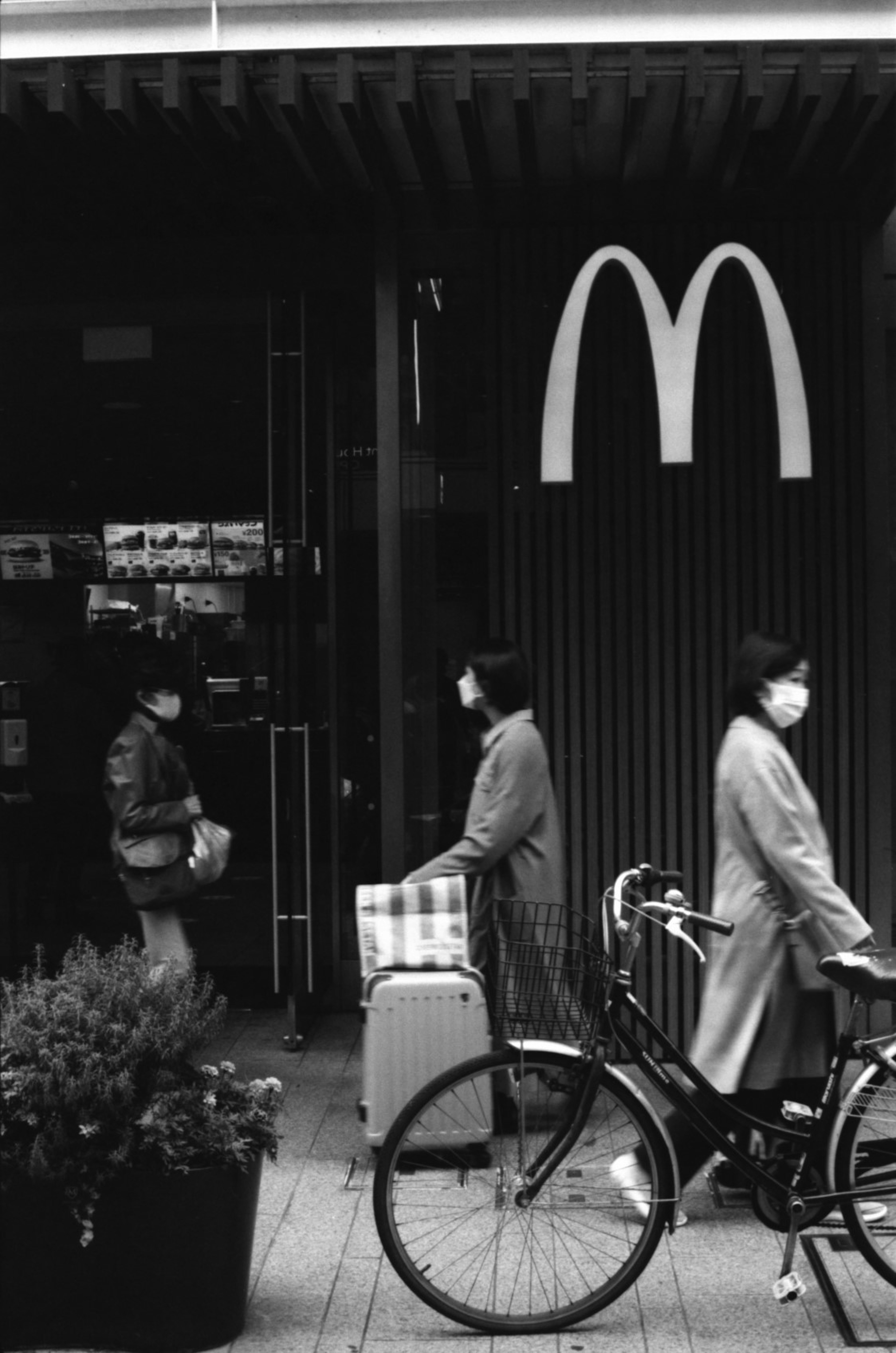 Due donne con maschere che camminano davanti all'ingresso di un McDonald's