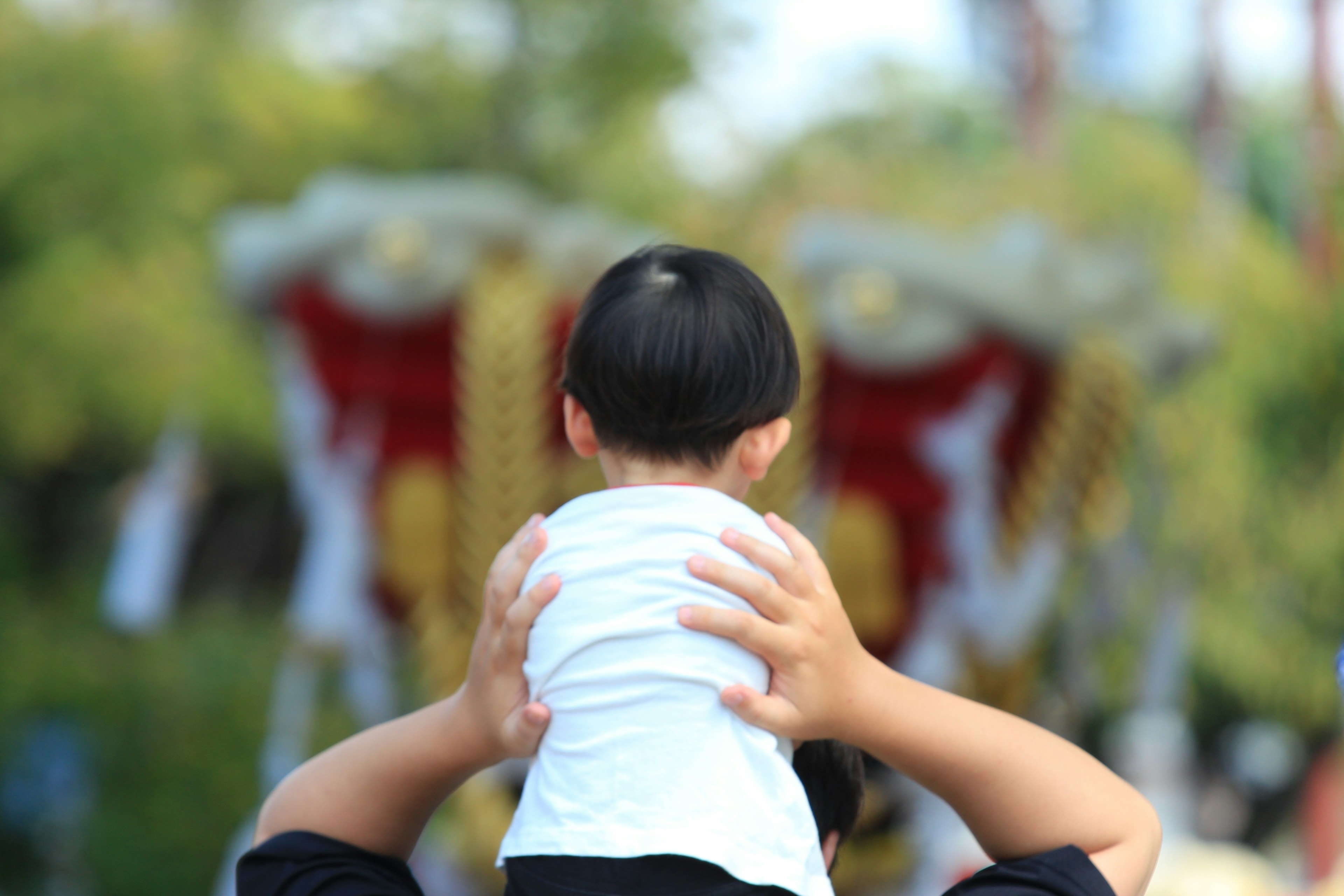 Adult carrying child on shoulders with lion dance in background