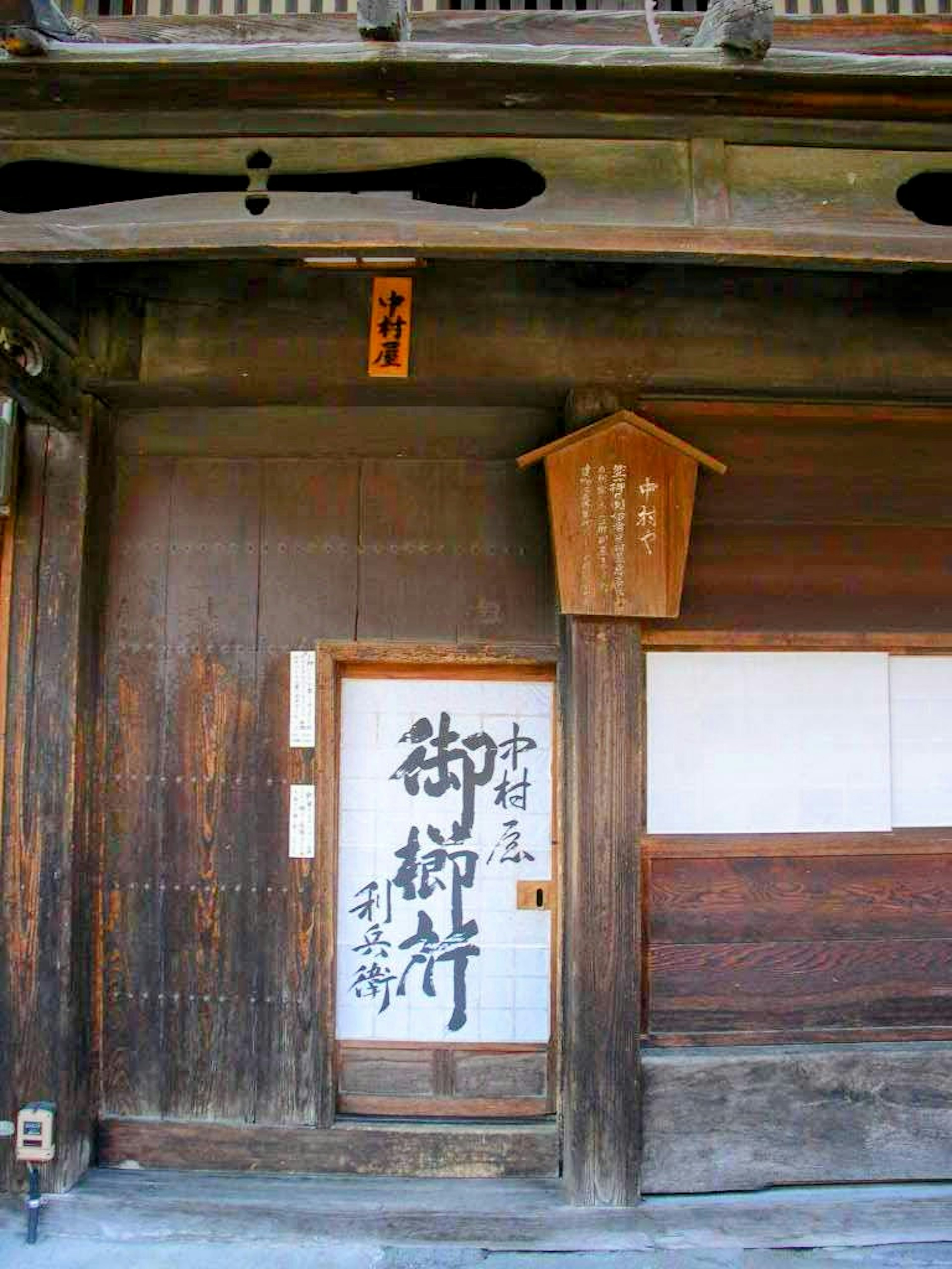 Eingang eines traditionellen japanischen Holzhauses mit einem geschriebenen Schild und einer Tür