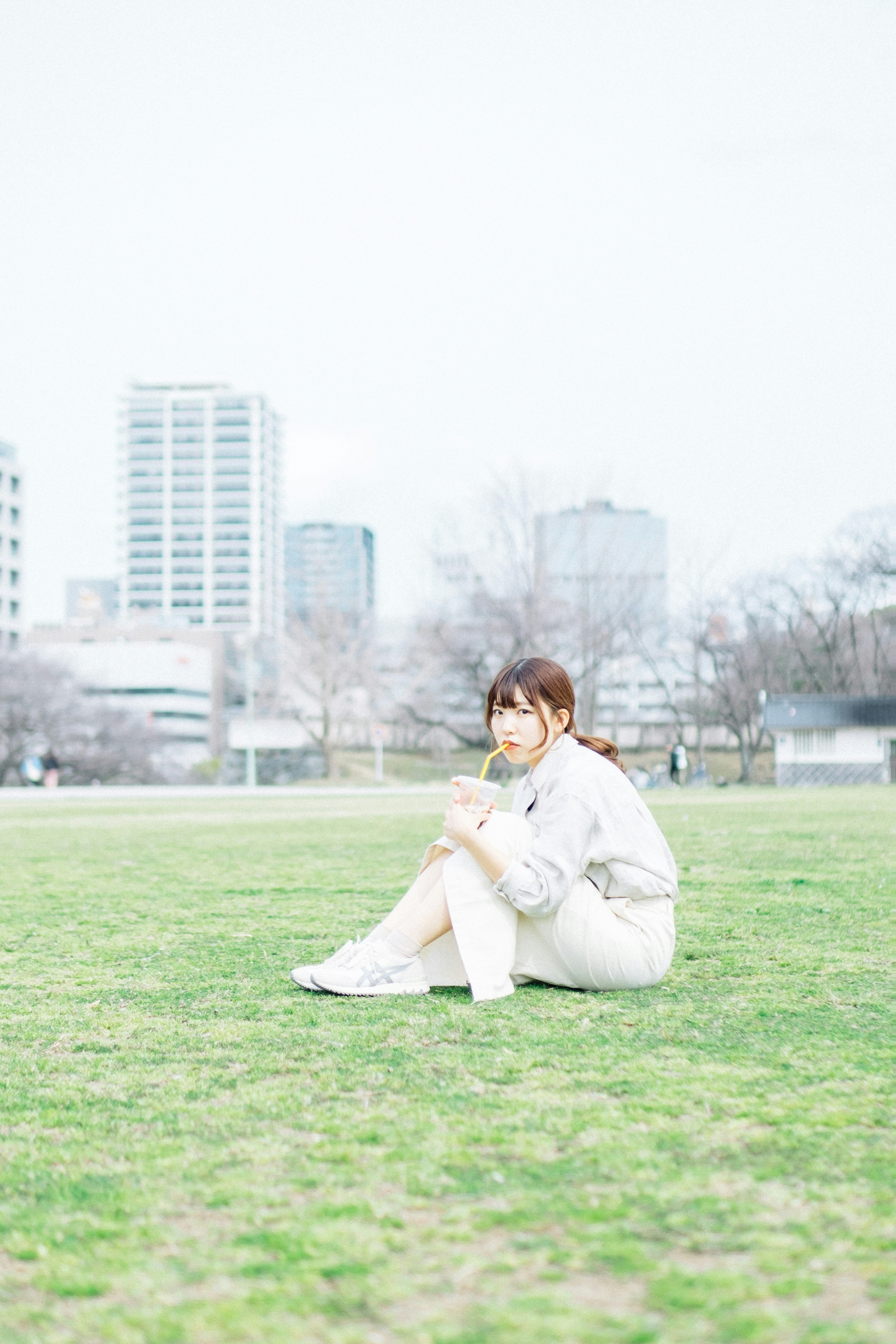 A woman in white clothing sitting on grass in a park