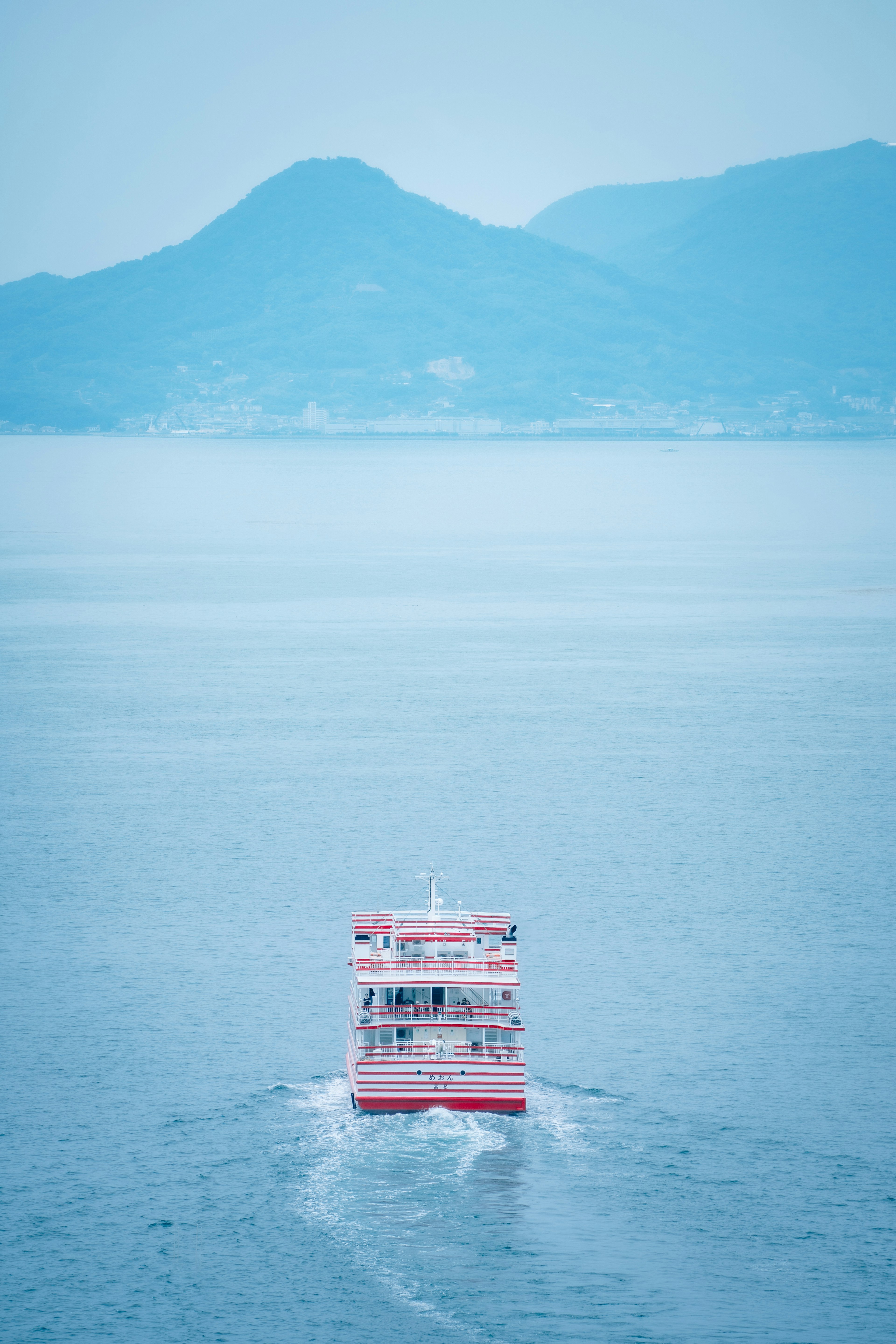 Barco rojo navegando en agua azul con montañas al fondo