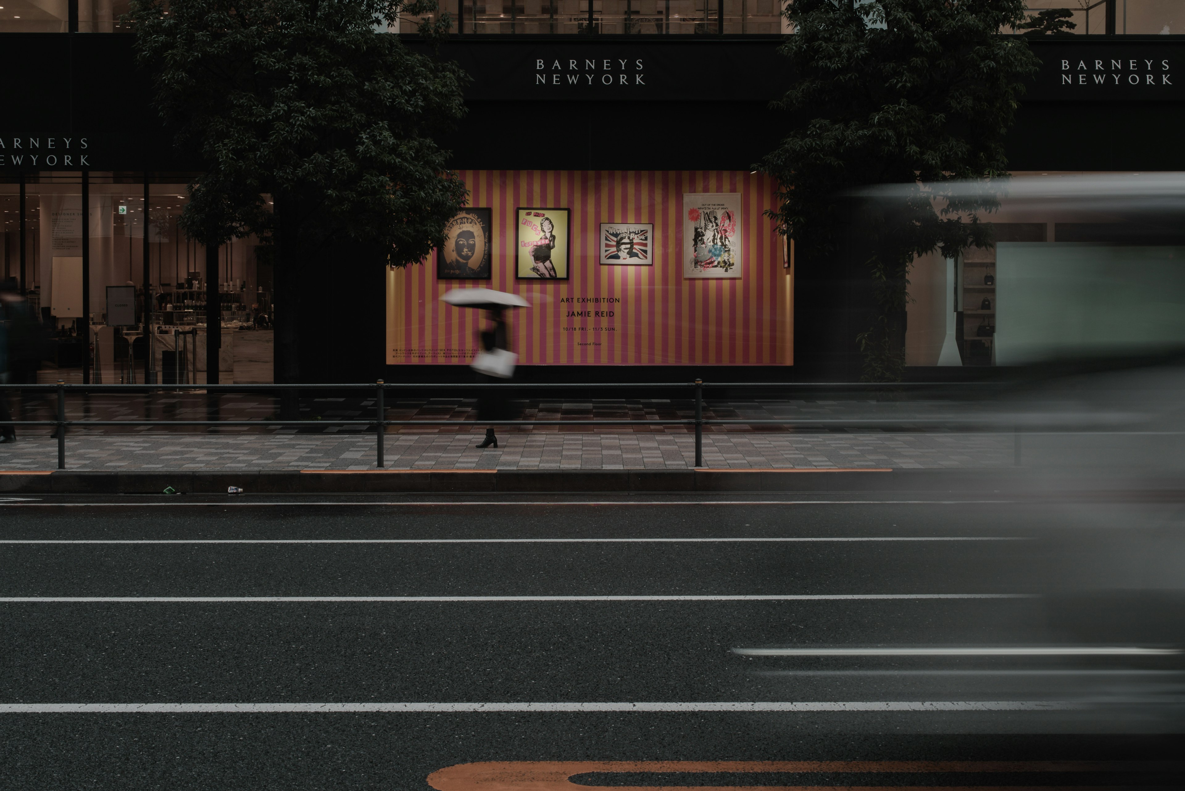 A person walking with an umbrella in the rain in front of a store