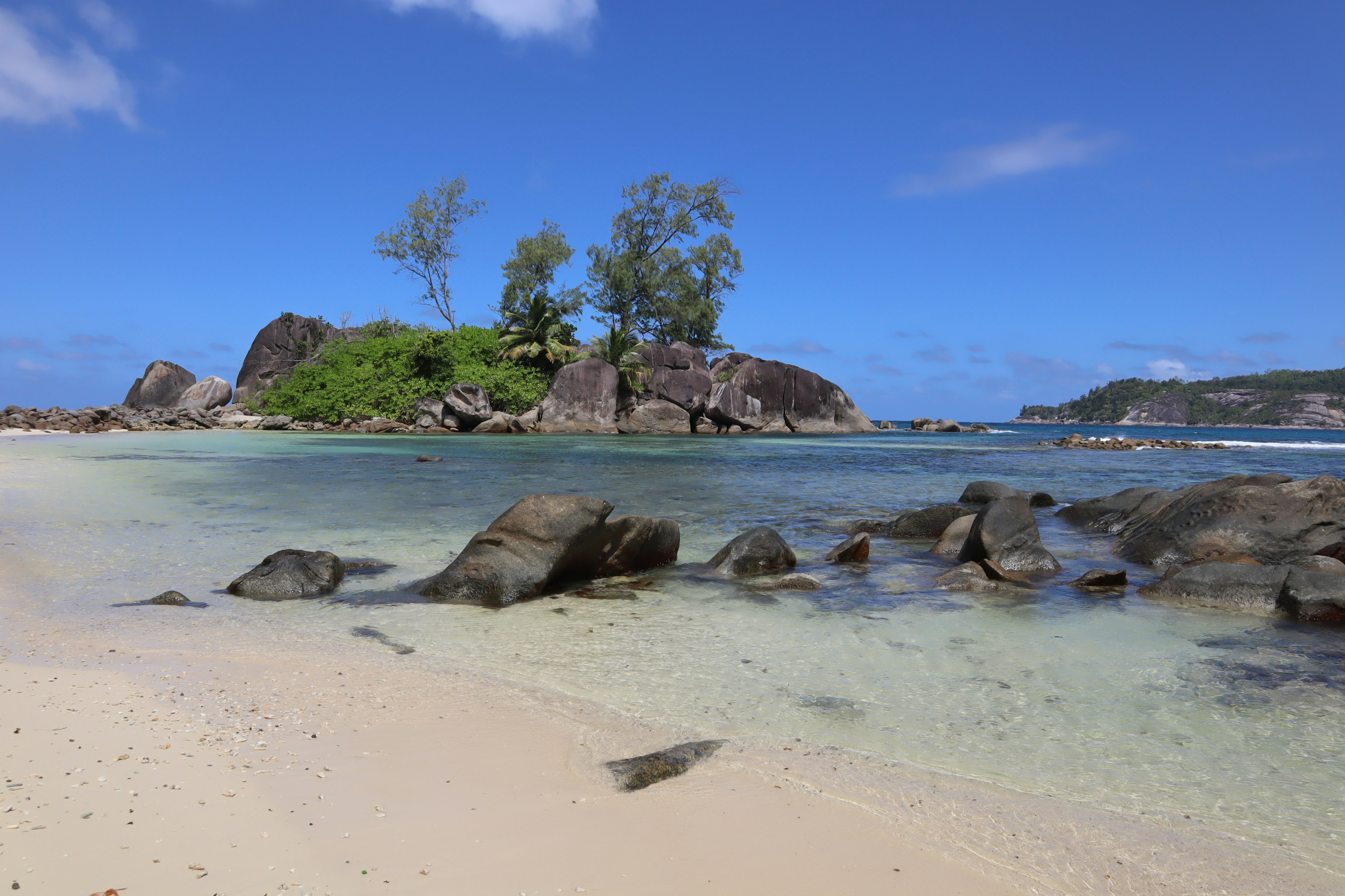 ทิวทัศน์ชายหาดที่สวยงามพร้อมท้องฟ้าสีฟ้าและทรายขาวล้อมรอบด้วยน้ำตื้นและก้อนหิน