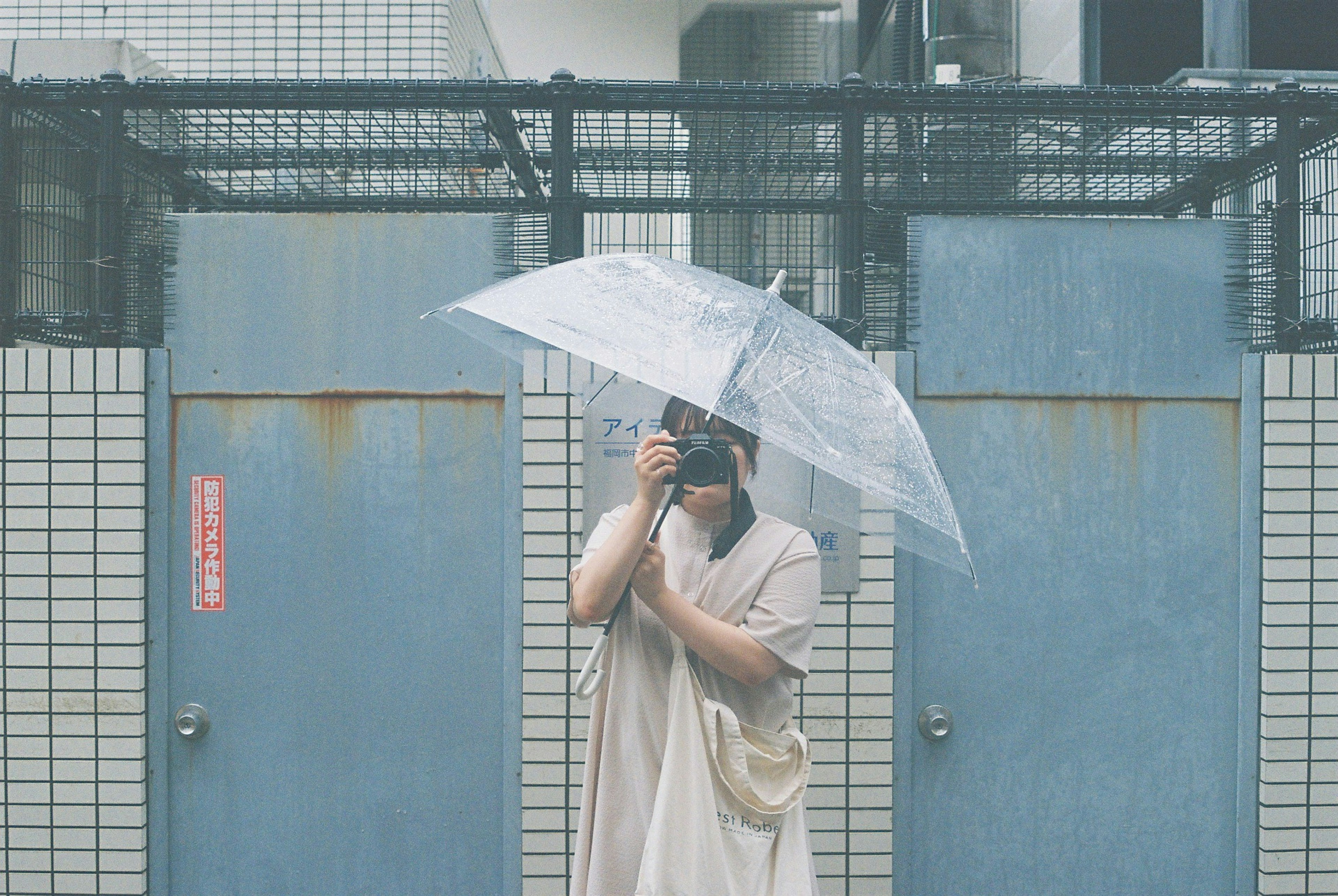 雨の中でカメラを持っている人物と透明な傘