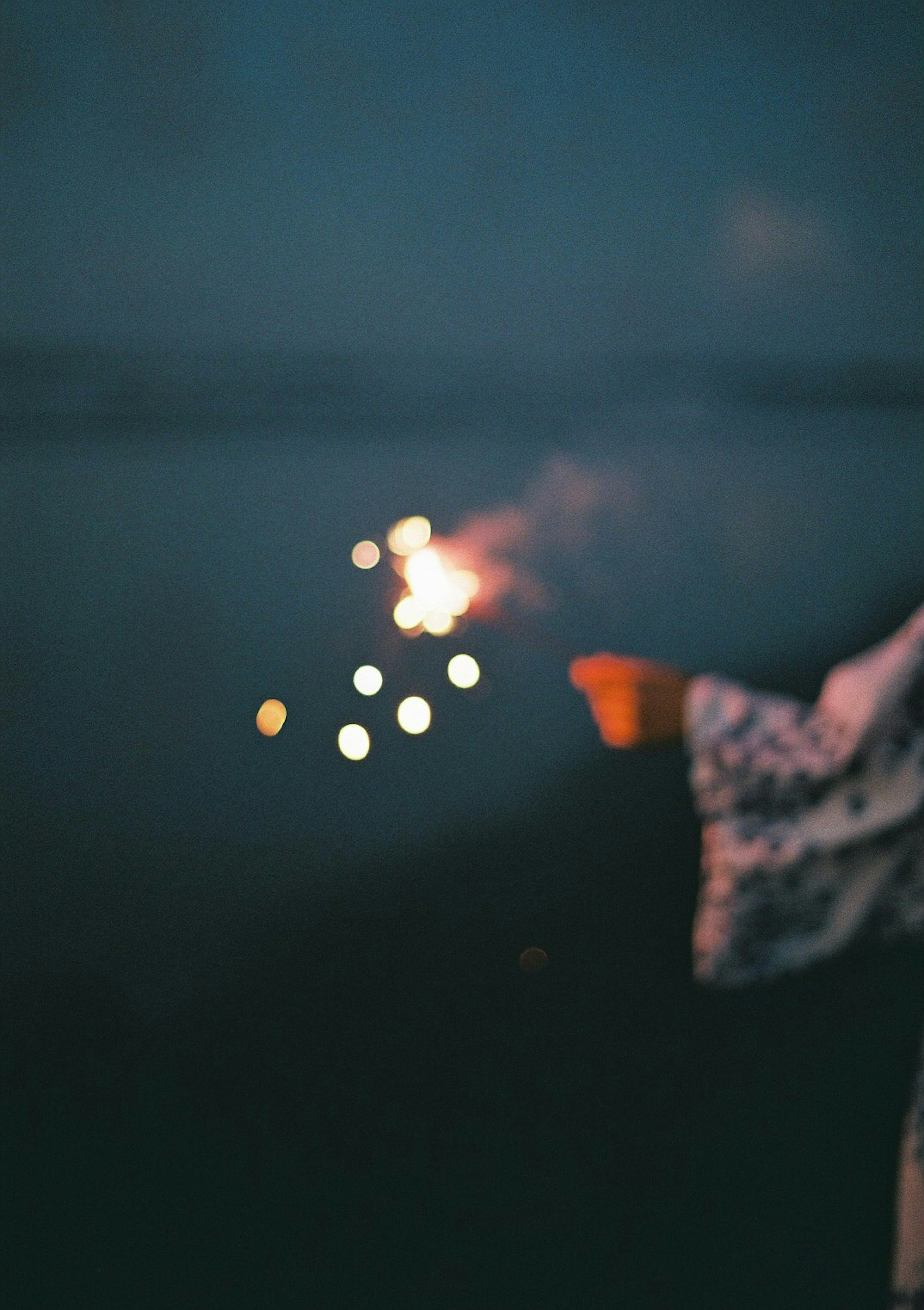 A hand holding a sparkler against a dark lake background