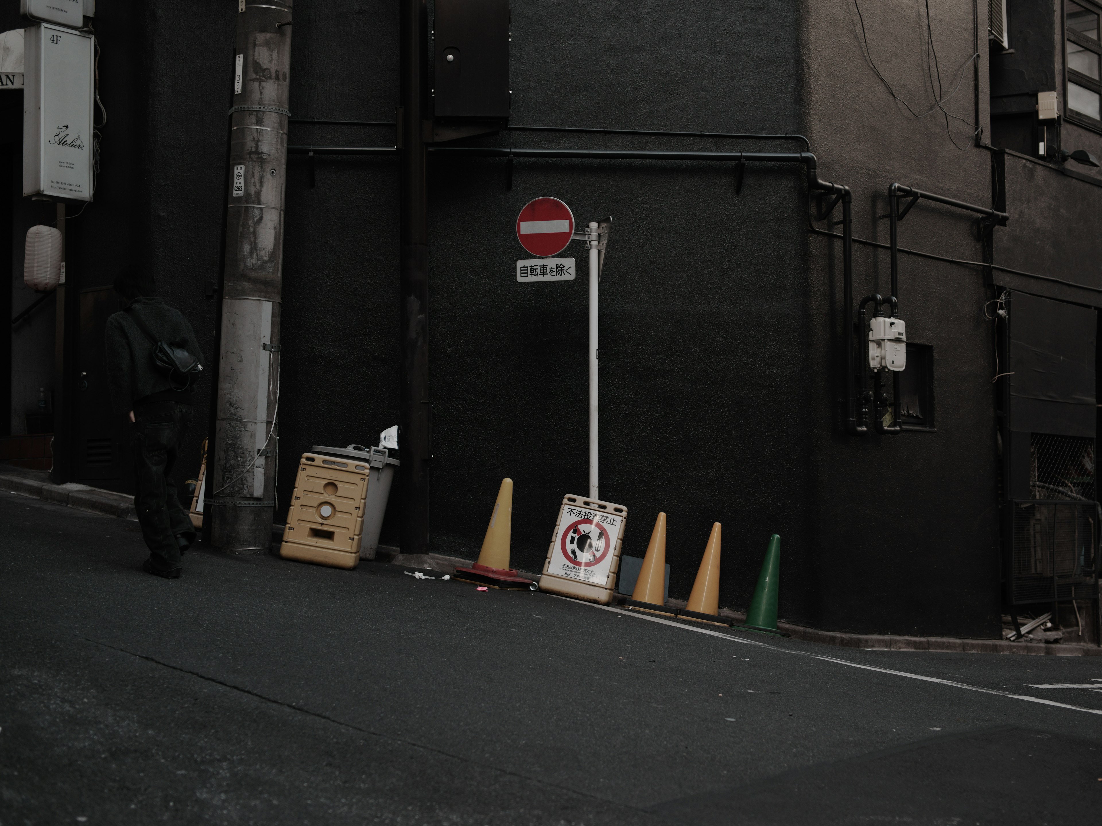 Una escena de calle inclinada con un edificio negro y un letrero de prohibición de entrada junto a conos de tráfico