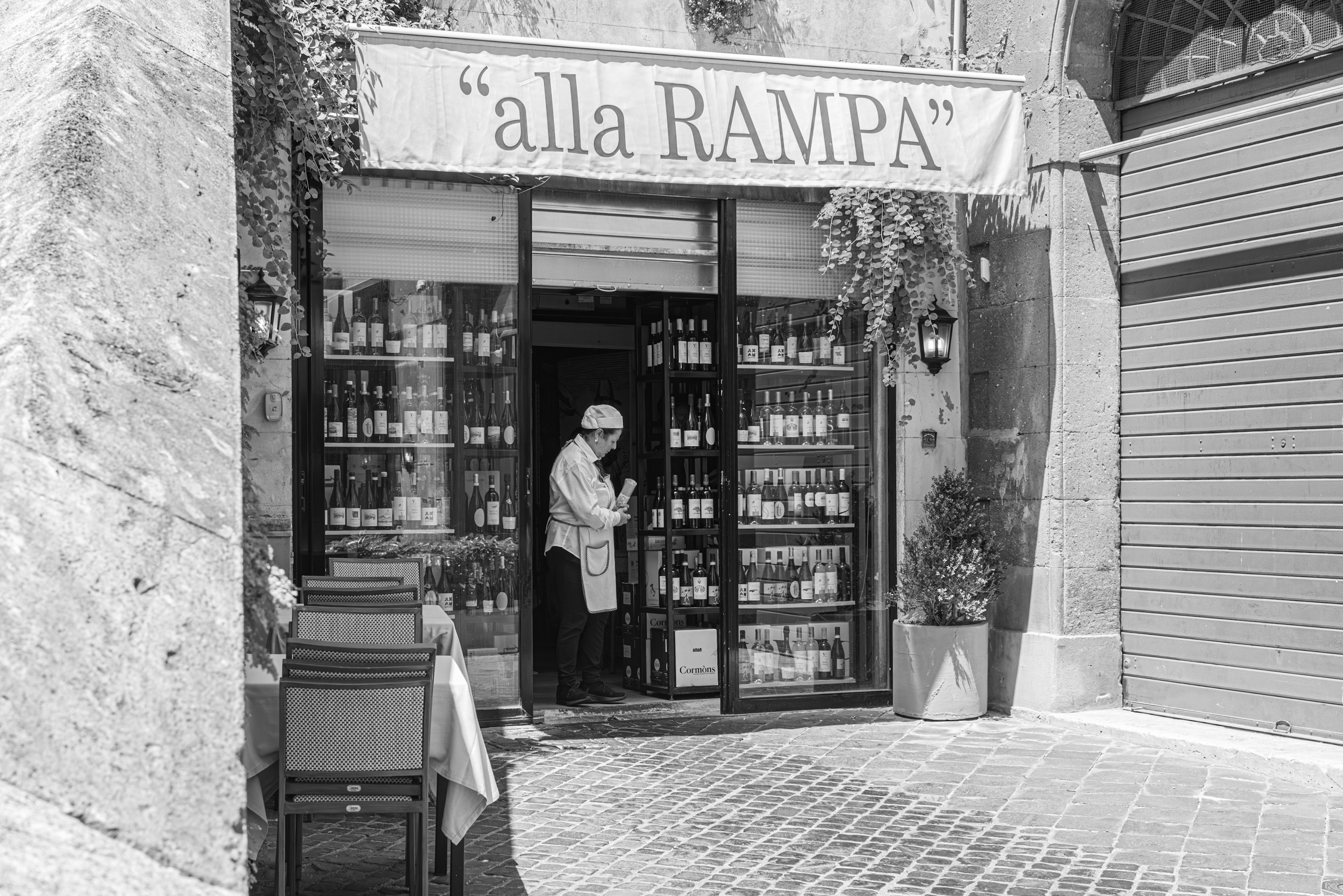 Immagine in bianco e nero di un piccolo negozio chiamato 'alla RAMPA' con un membro del personale all'interno