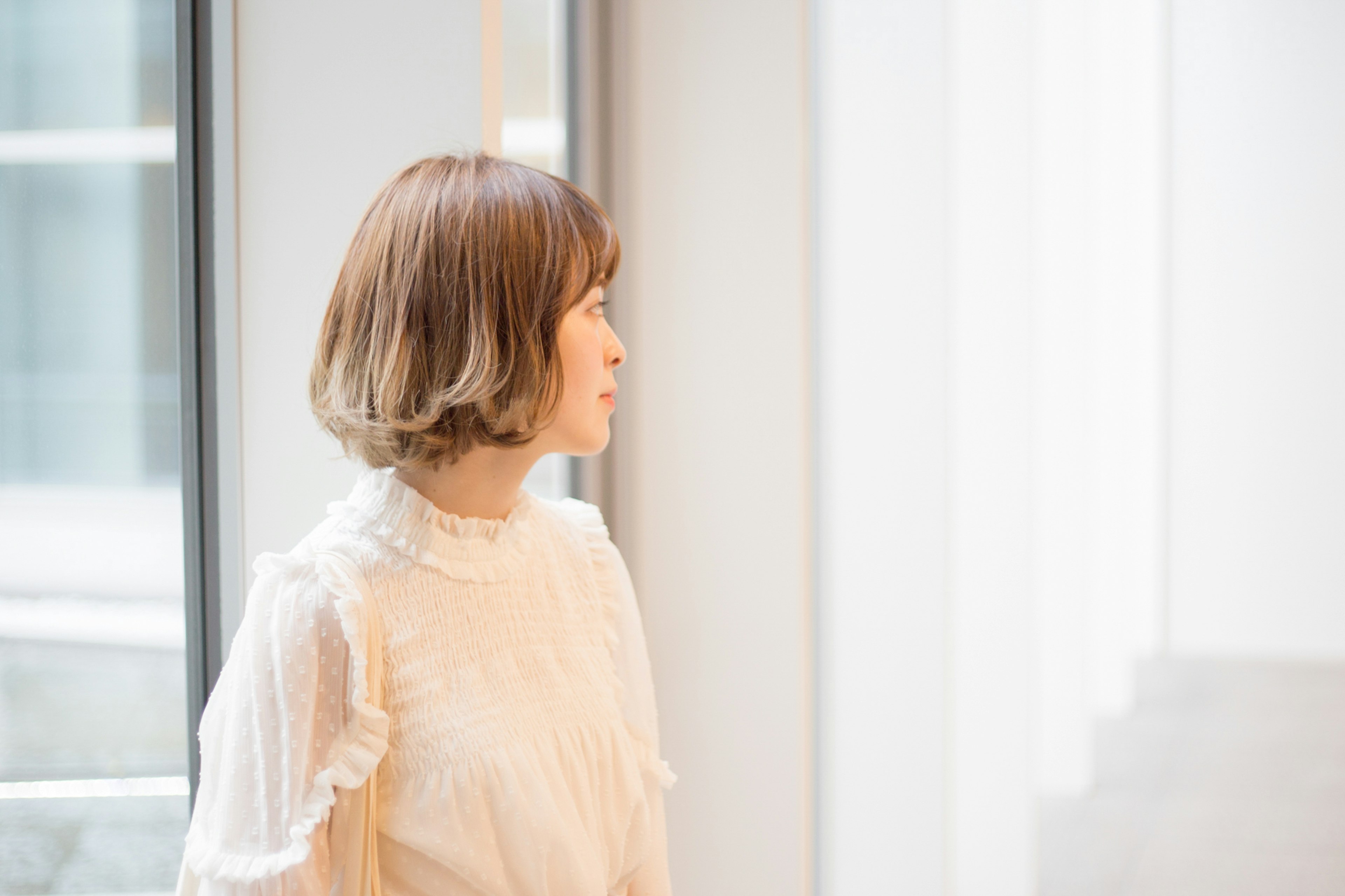 Side profile of a woman standing near a window soft light illuminating her natural expression wearing a ruffled white blouse