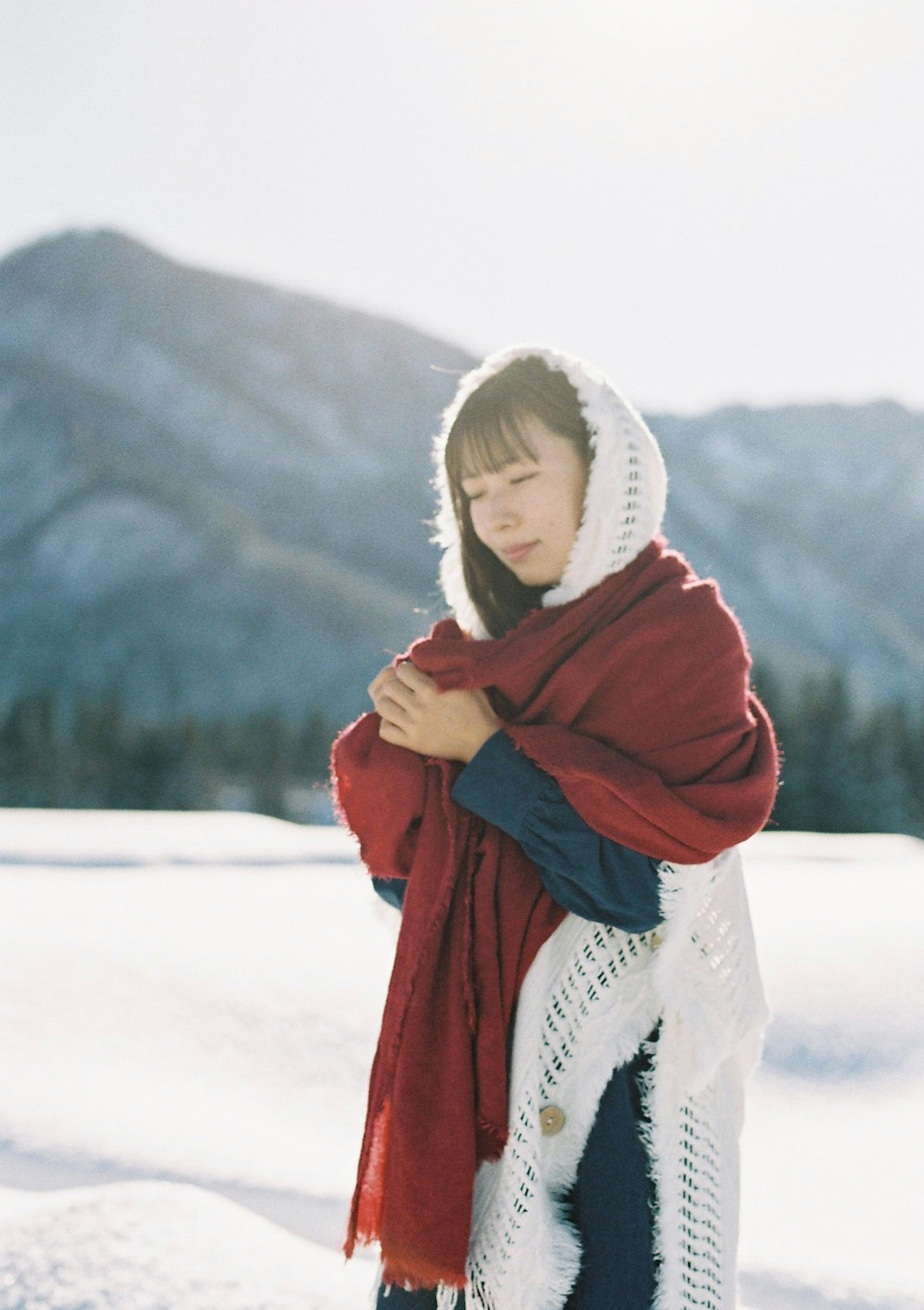 一位穿著紅色披肩的女性在雪中站立，背景是山脈